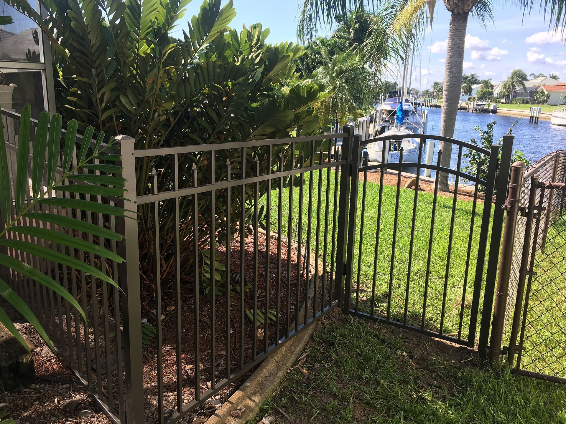 Black metal fence with a gate, green grass, and water in the background.