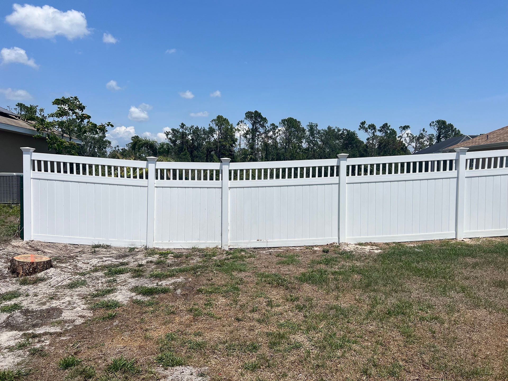White vinyl privacy fence in a grassy yard under a blue sky.