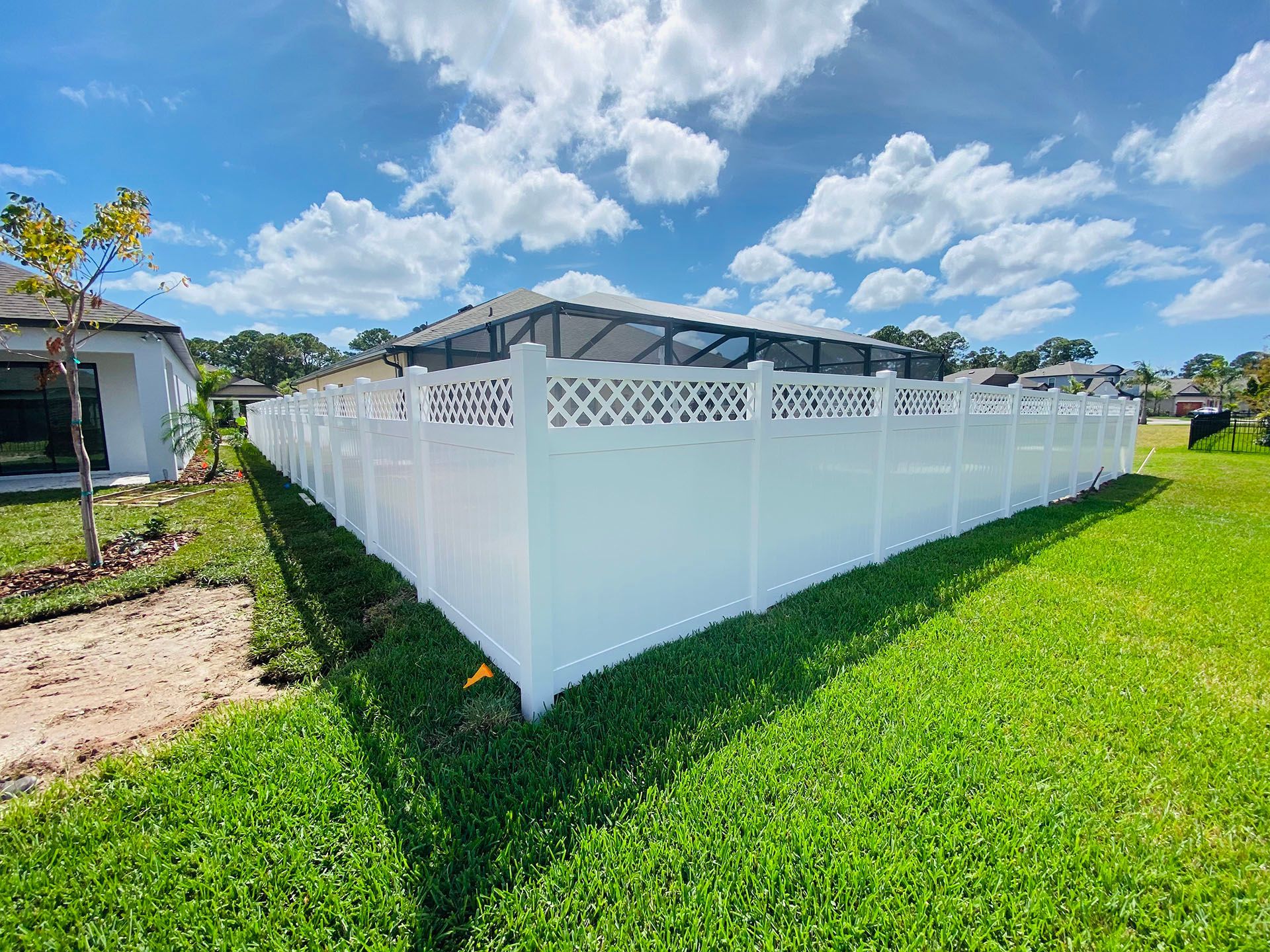 White vinyl fence surrounding a backyard with a pool. Sunny day, blue sky, and green grass.