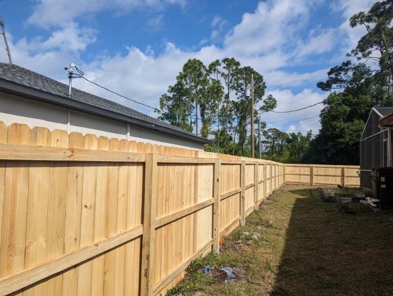 Wooden fence alongside a light-colored house under a cloudy sky.