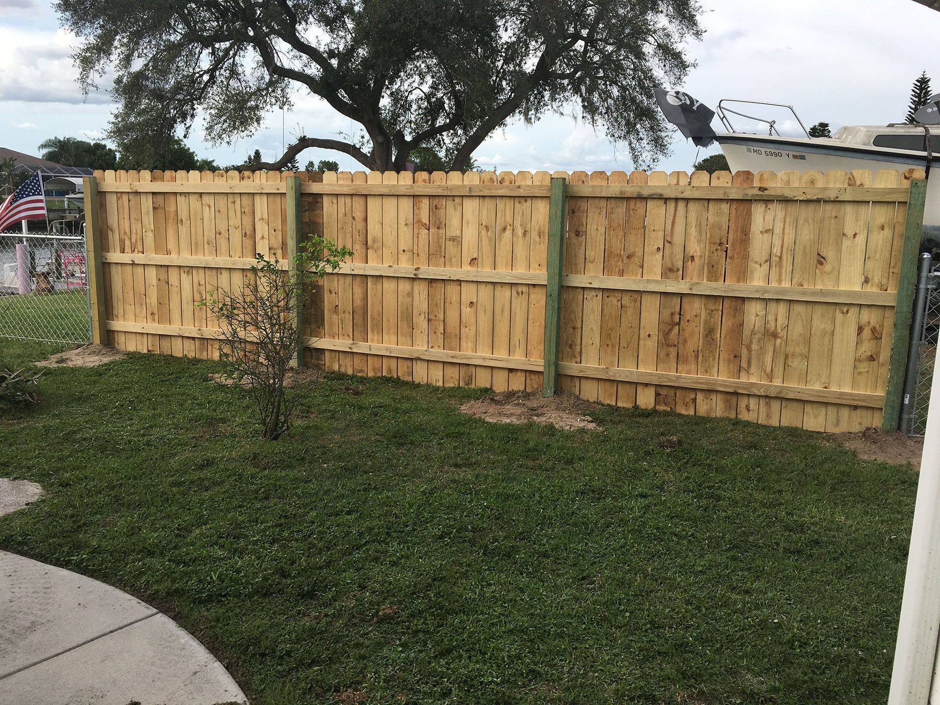 Wooden fence in a yard with green grass, posts are green, and a large tree in the background.