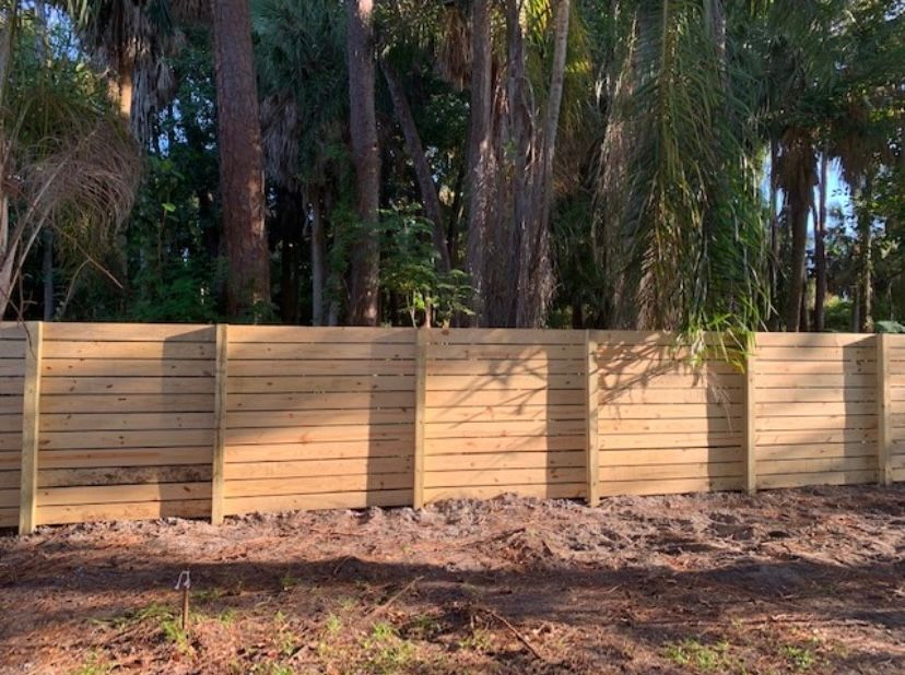 Wooden fence in front of trees, brown wood, sunny day.