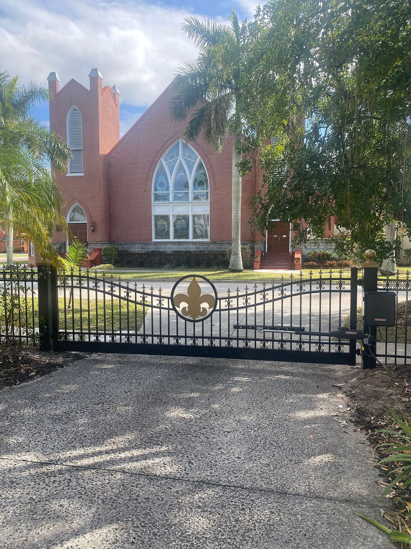 A brick church with a gated entrance. The gate has a fleur-de-lis emblem.