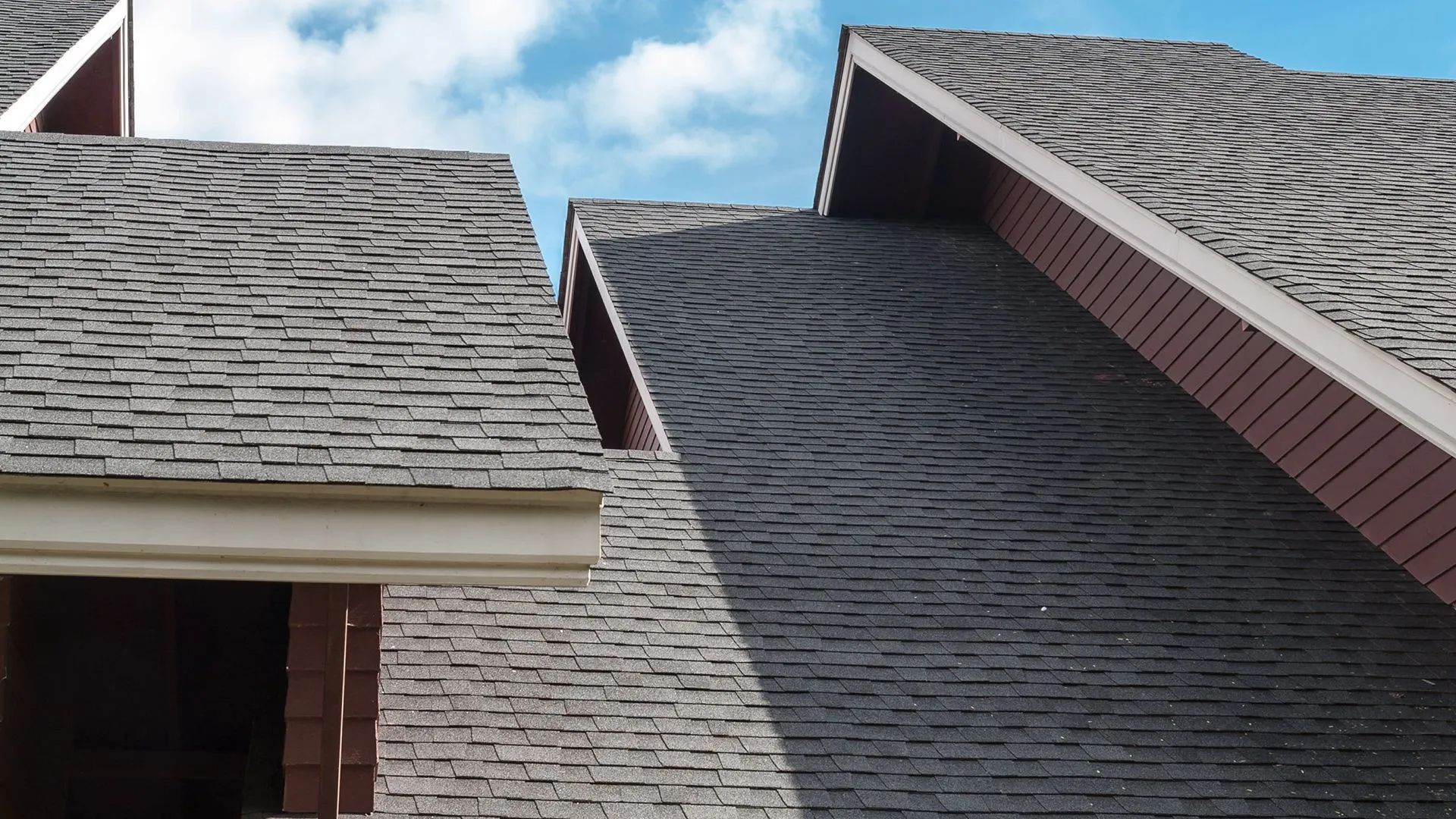Grey shingle roofs with red trim against a blue sky.