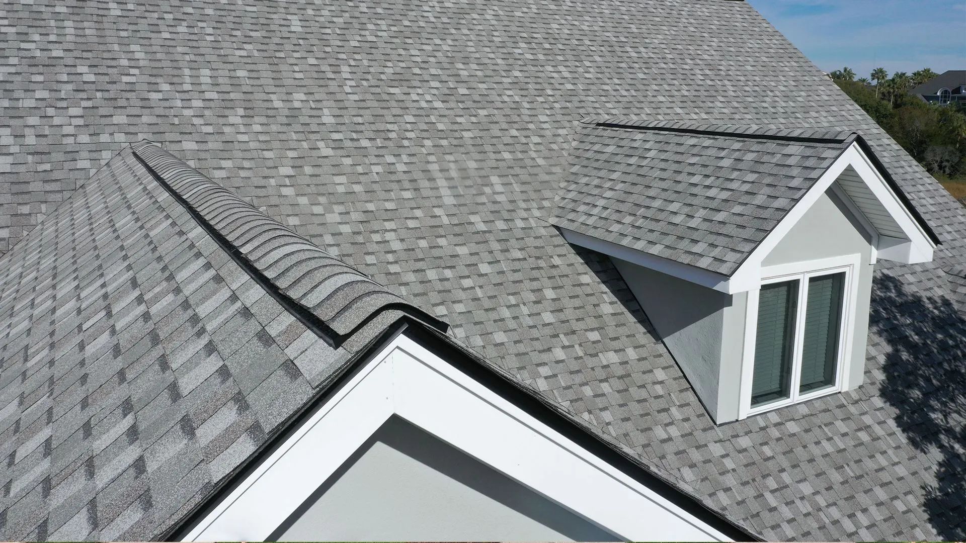 Gray shingle roof with a dormer and black trim against a blue sky.