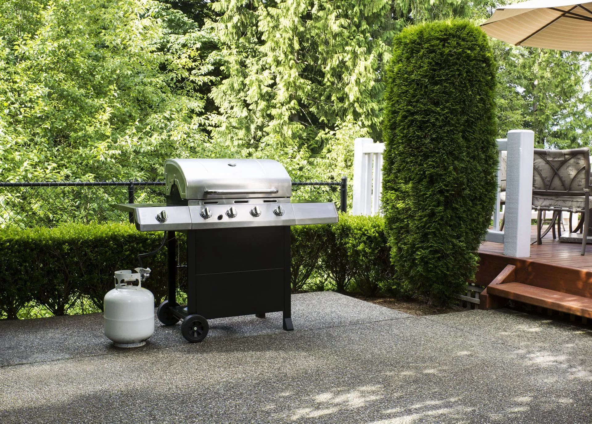 A gas grill is sitting on a patio next to a propane tank.