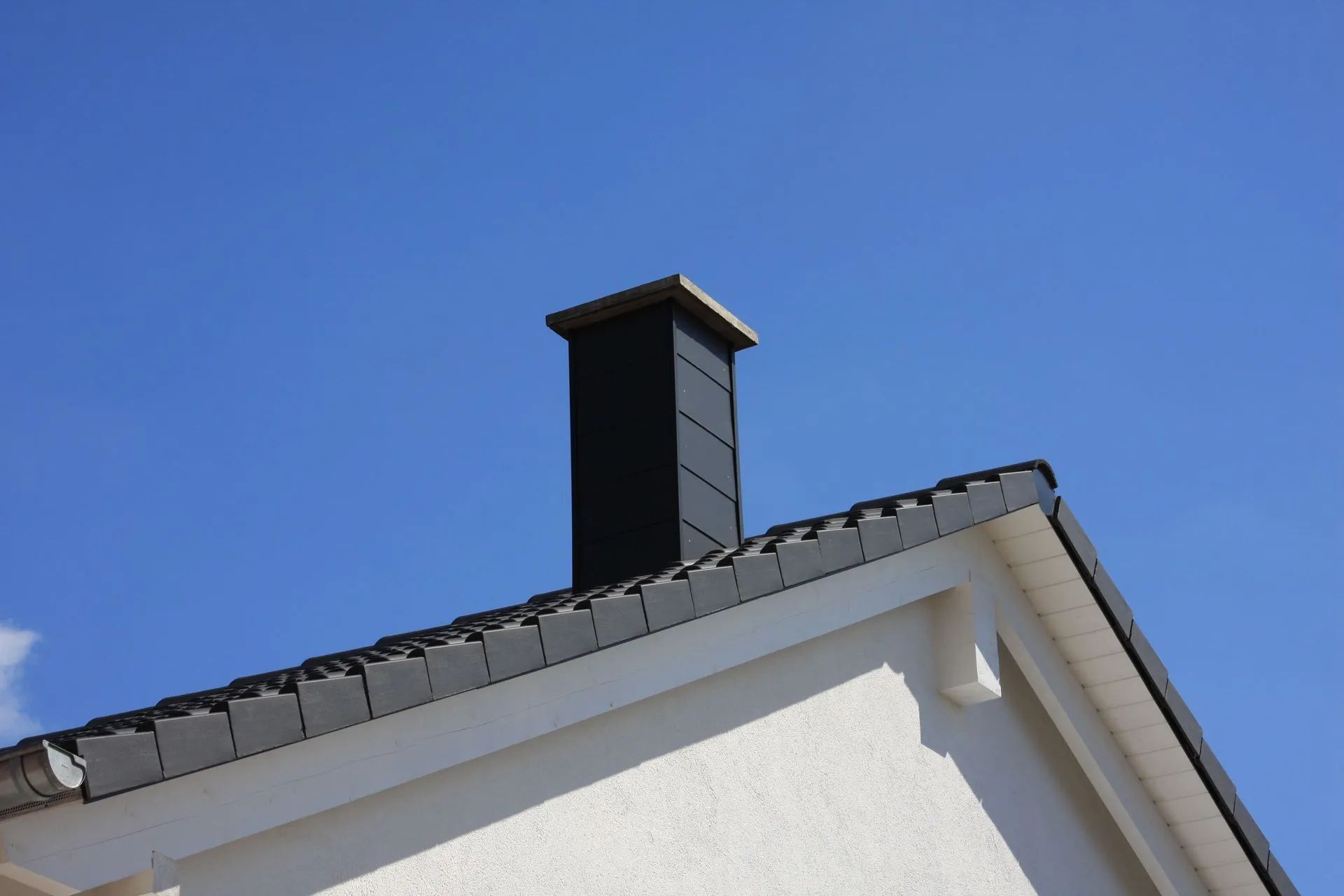 A chimney on top of a white house with a blue sky in the background