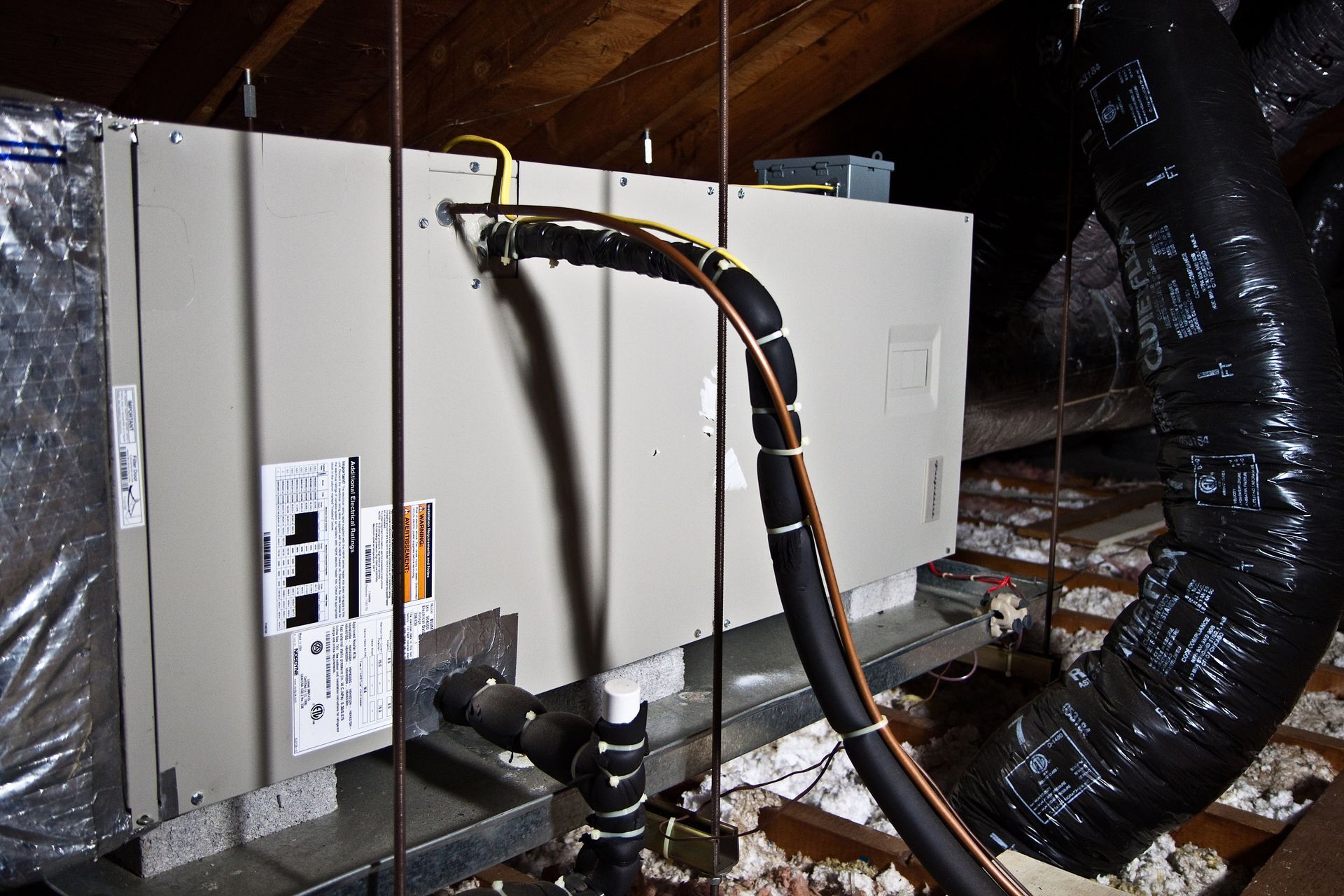 Basement HVAC unit with ductwork and pipes in an unfinished attic-like space.