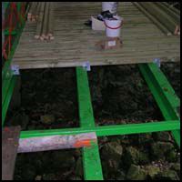 Small bamboo platform with bright green supports over a dark ground, holding a small container on top.