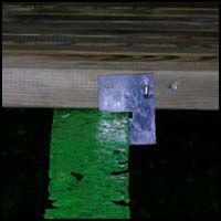 Close-up of a weathered wooden surface with a green paint-marked bracket and a small metal plate attached.