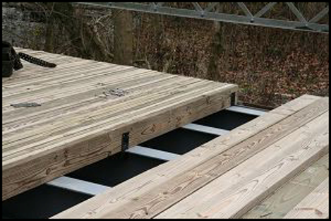 Wooden bridge deck panels being installed over black support beams outdoors