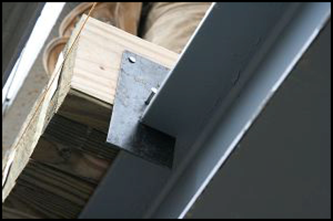 Metal bracket securing a dark beam to a wooden beam under a construction structure