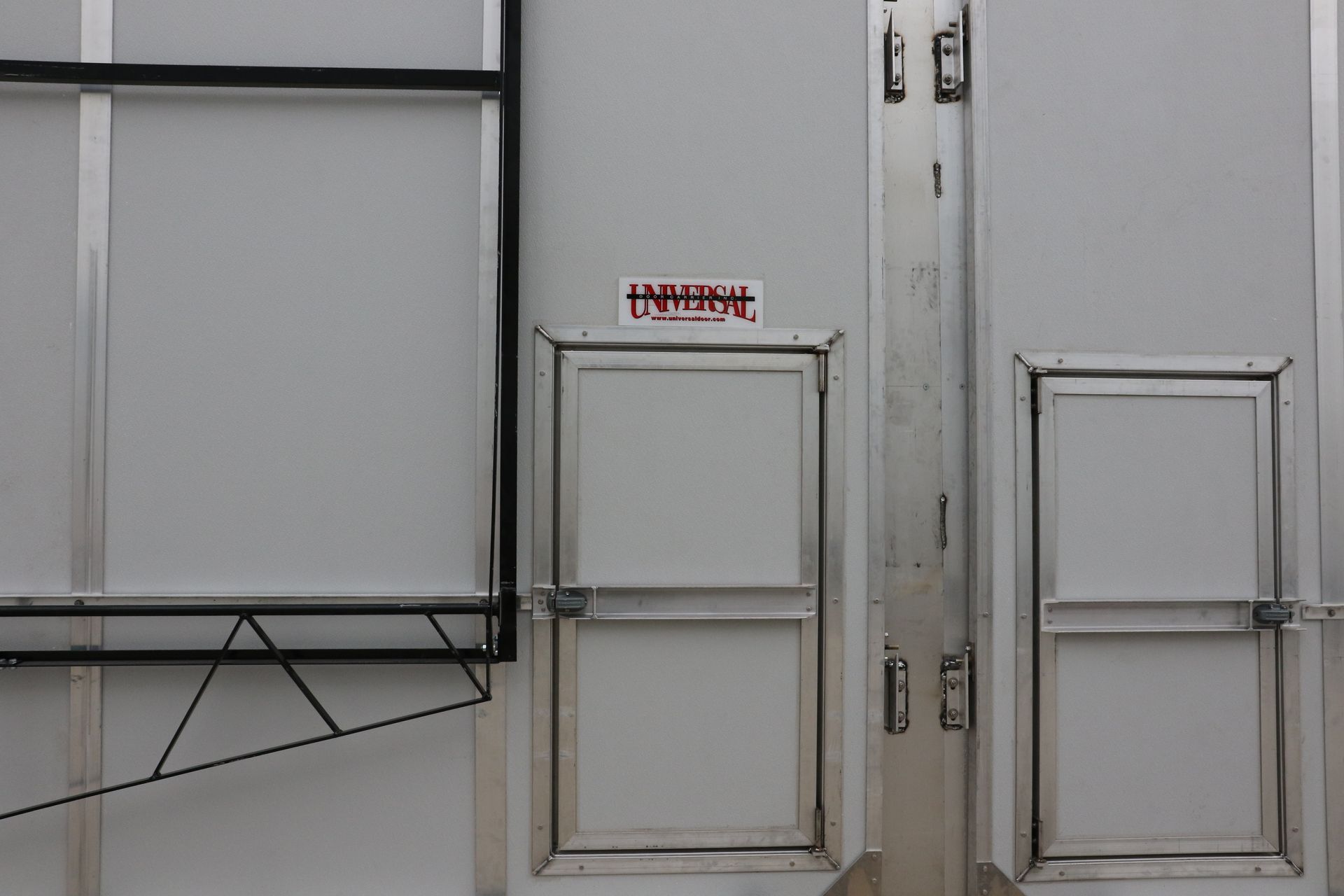 White metal doors and a wall-mounted shelf in a plain industrial room with a small red sign above the center door