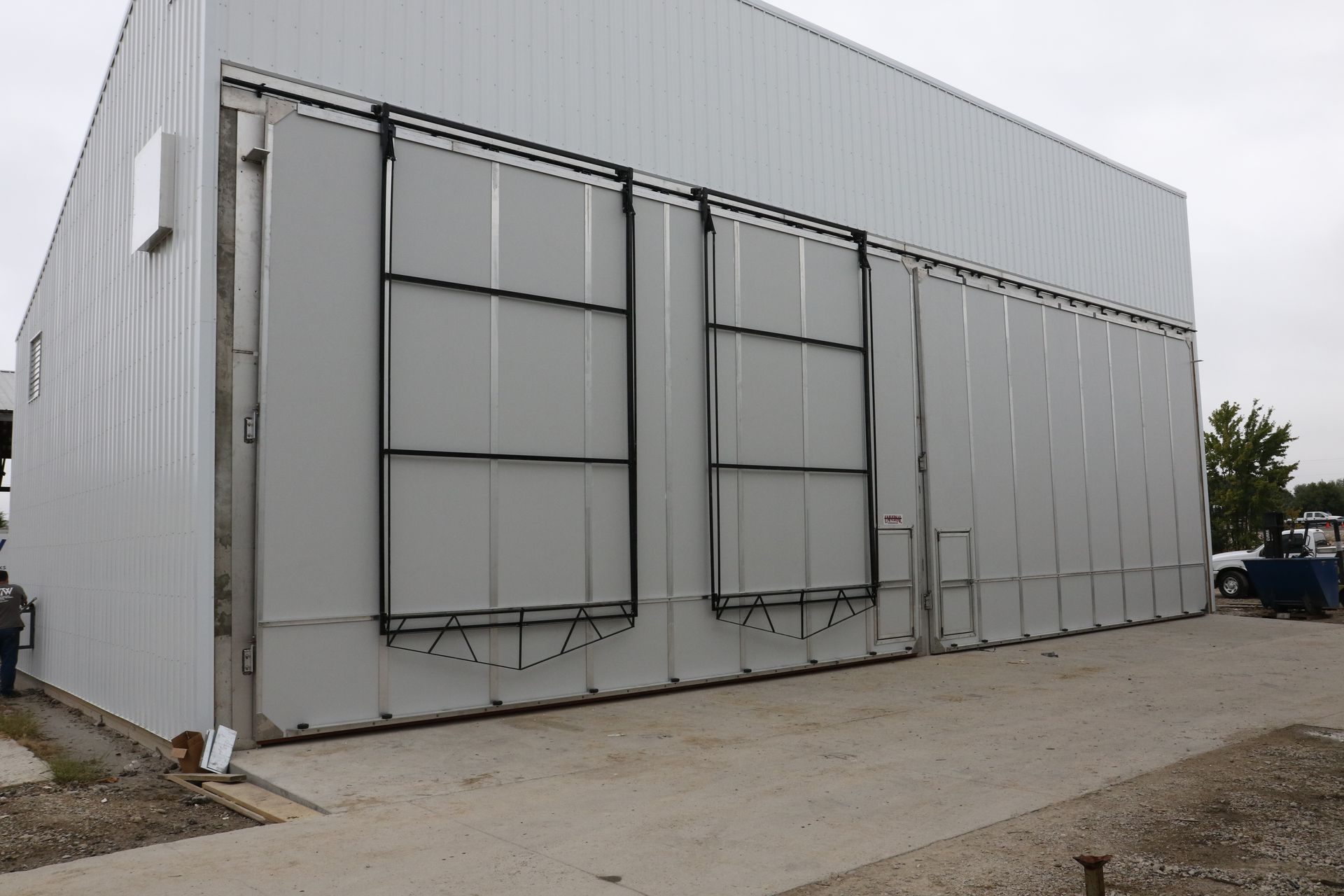 Large gray industrial building with several tall panel doors on a concrete lot