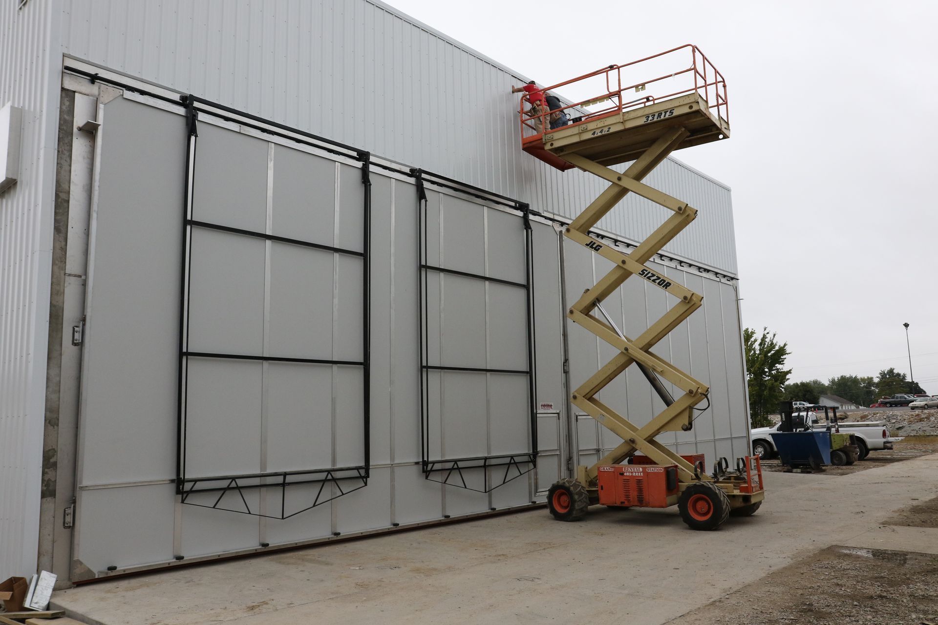 Scissor lift raised beside a large gray industrial building wall with tall panels and a red platform