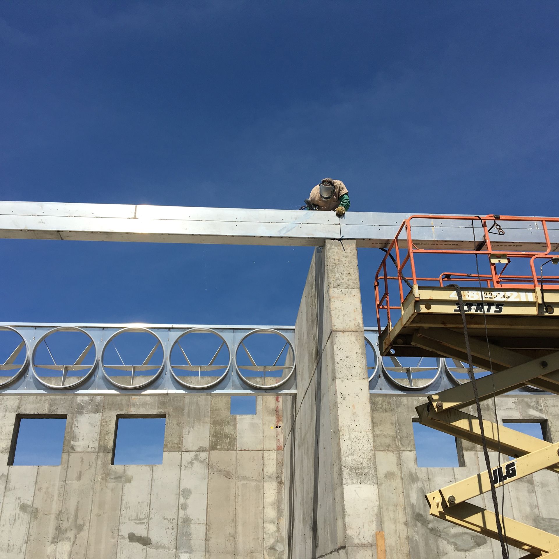 Construction worker atop concrete beam on building frame under a blue sky