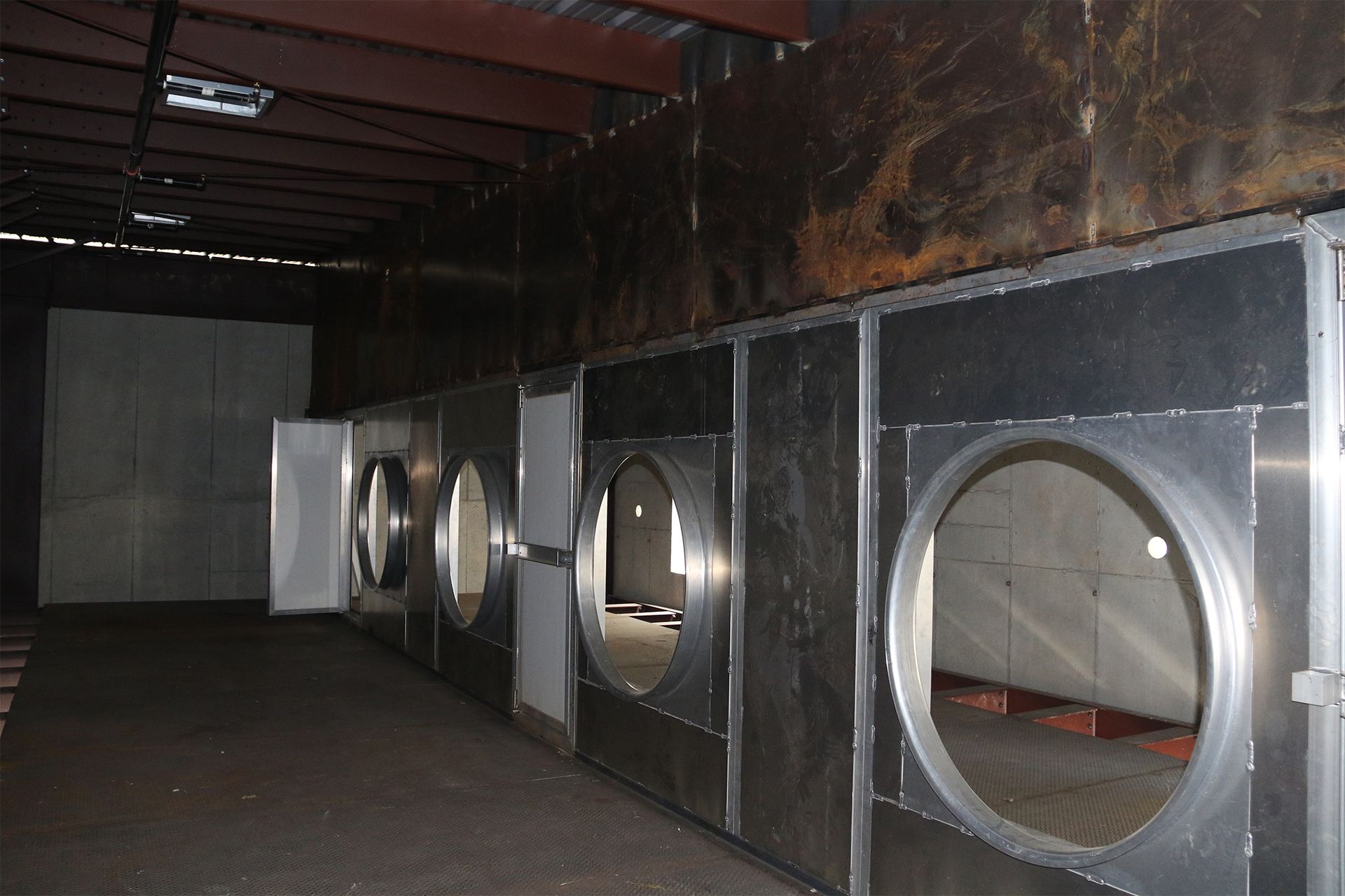 Row of large metal ventilation ducts inside a dim industrial room