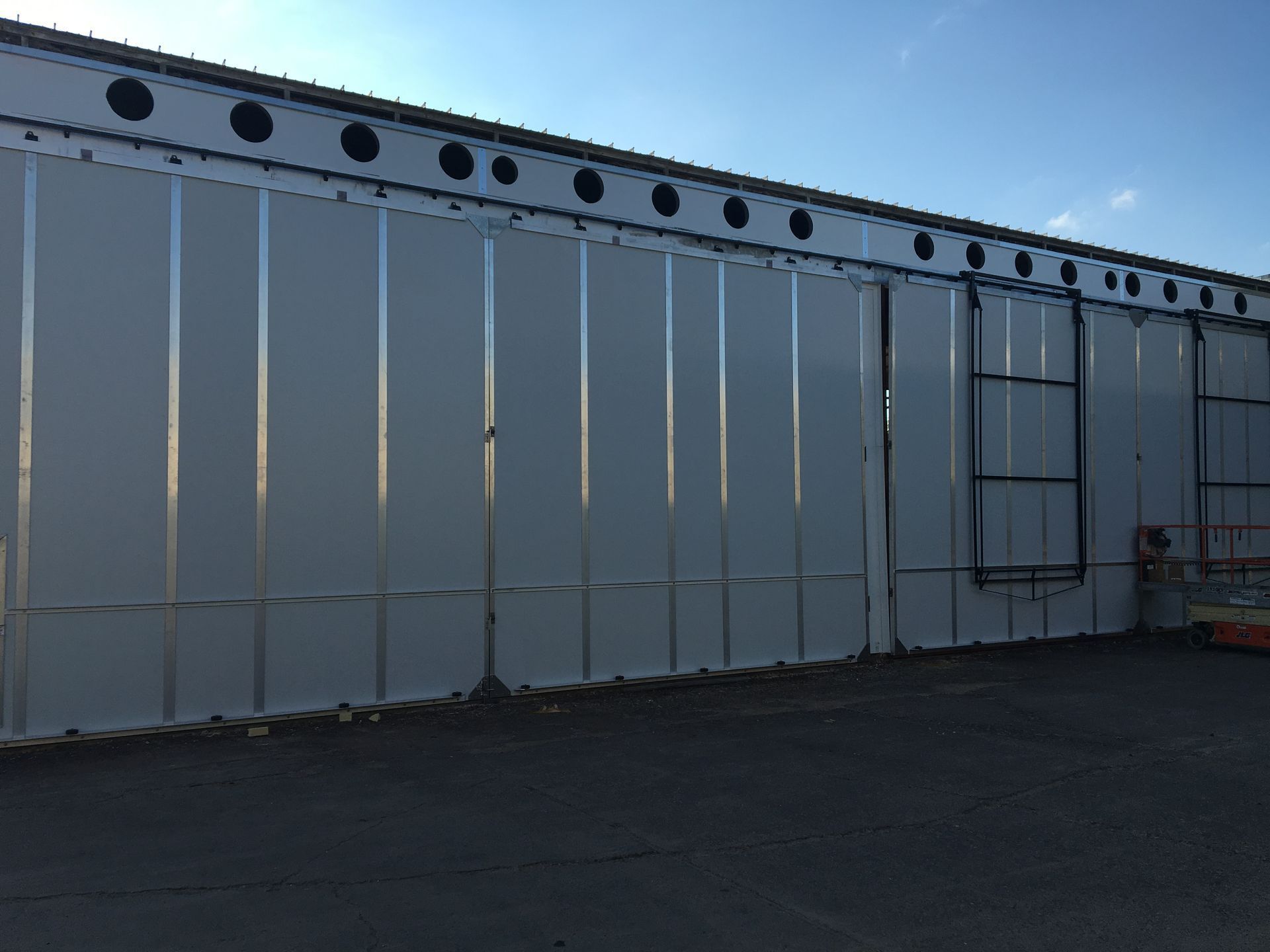 Gray industrial building wall with vertical panels and circular vents along the roofline at dusk