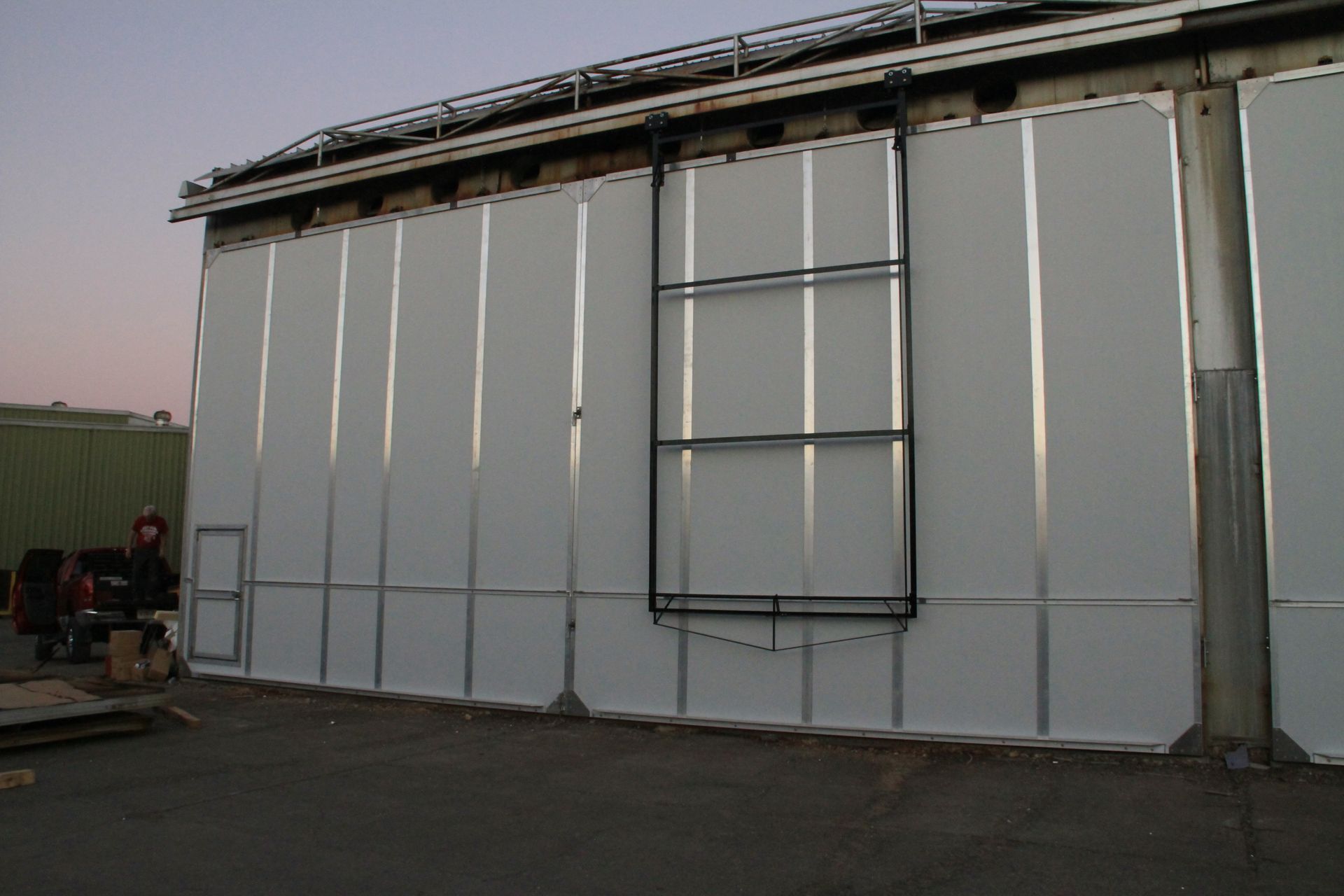 Large white industrial building wall with a metal scaffold frame in front and an open roof edge above