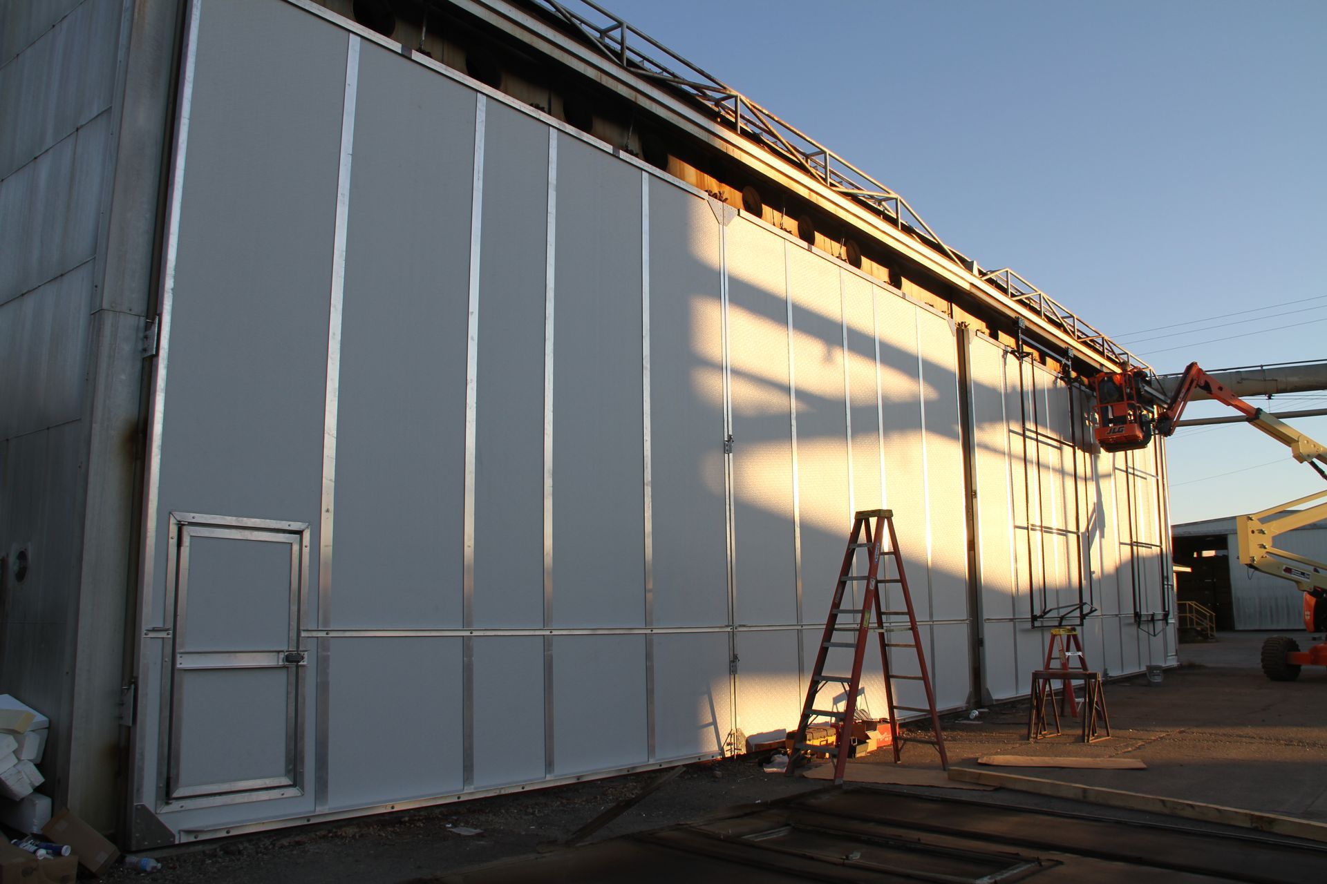 Large white building wall with ladders and a cherry picker at a construction site during sunset