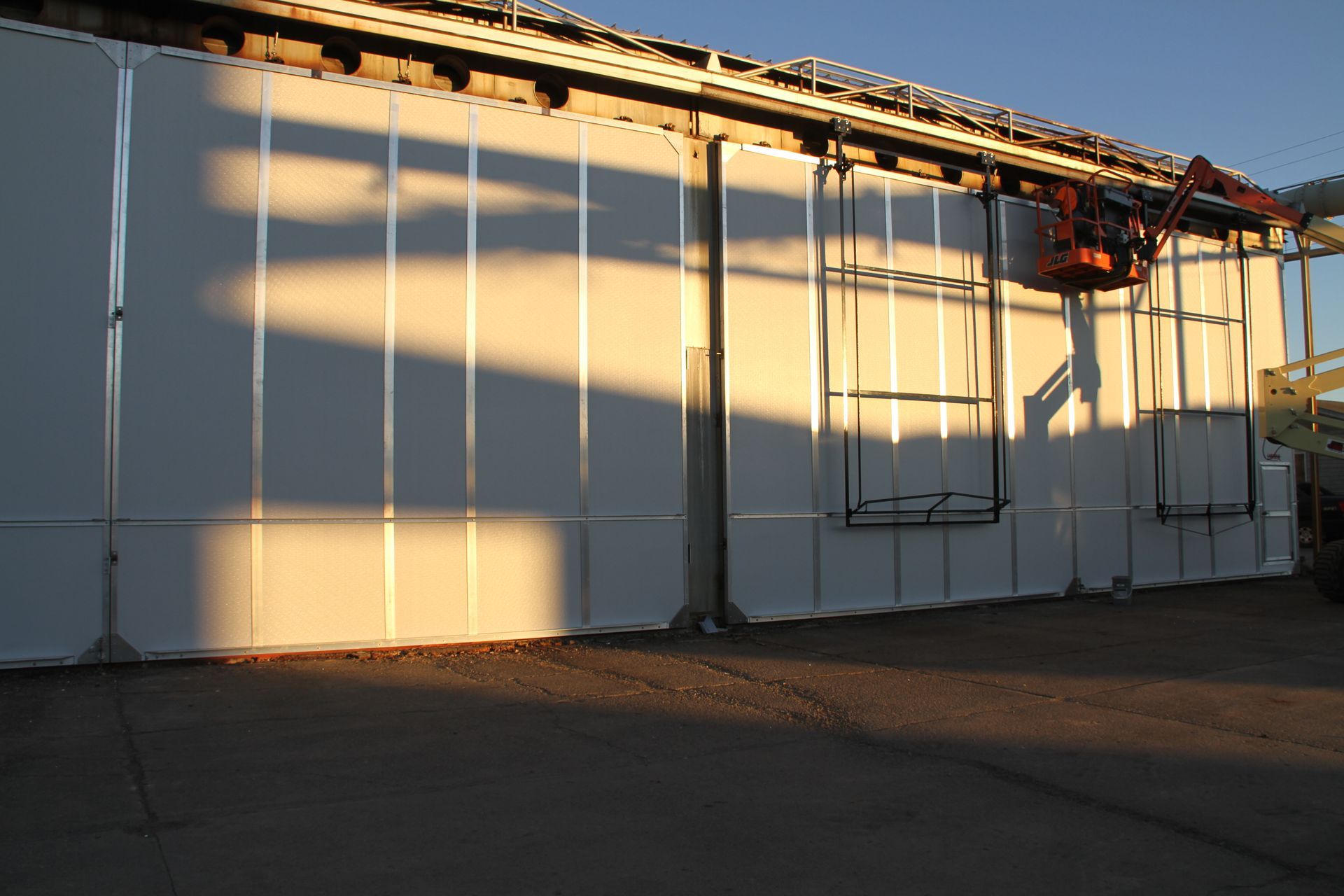 Sunlit white industrial building with long shadows on a paved lot