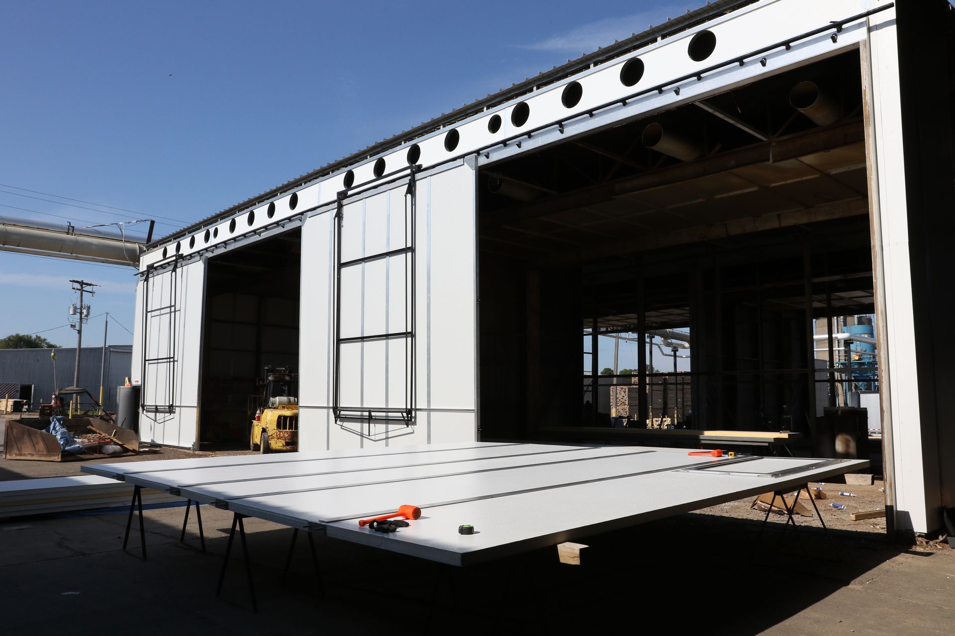Industrial building under construction with metal walls, open doorway, and a raised platform in front