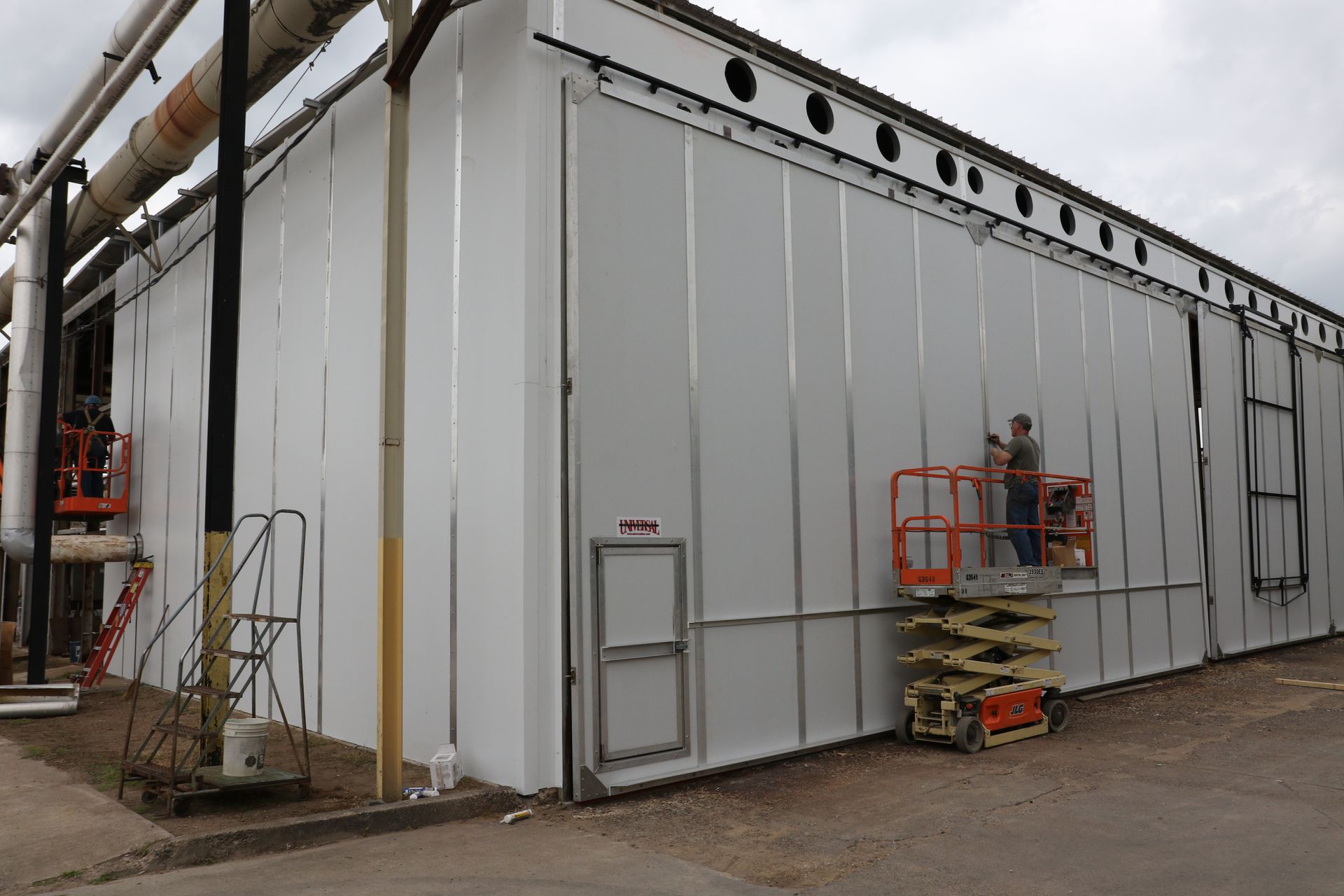 Gray industrial building with workers on orange lifts near an exterior wall