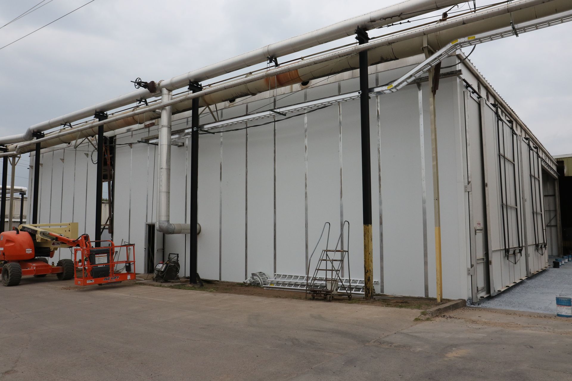 Large white industrial tent structure with metal support poles and pipes on a paved lot
