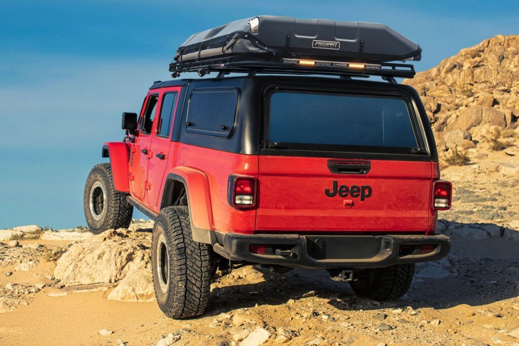 a red jeep with a tent on top of it is driving down a dirt road .