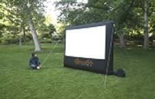 A person is sitting in front of a large inflatable screen in a park.