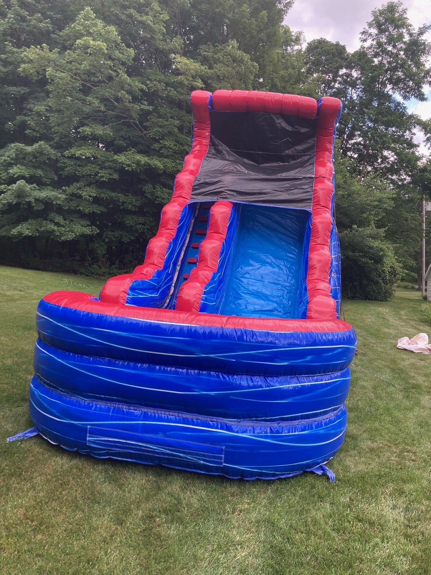 A blue and red inflatable water slide is sitting on top of a lush green field.