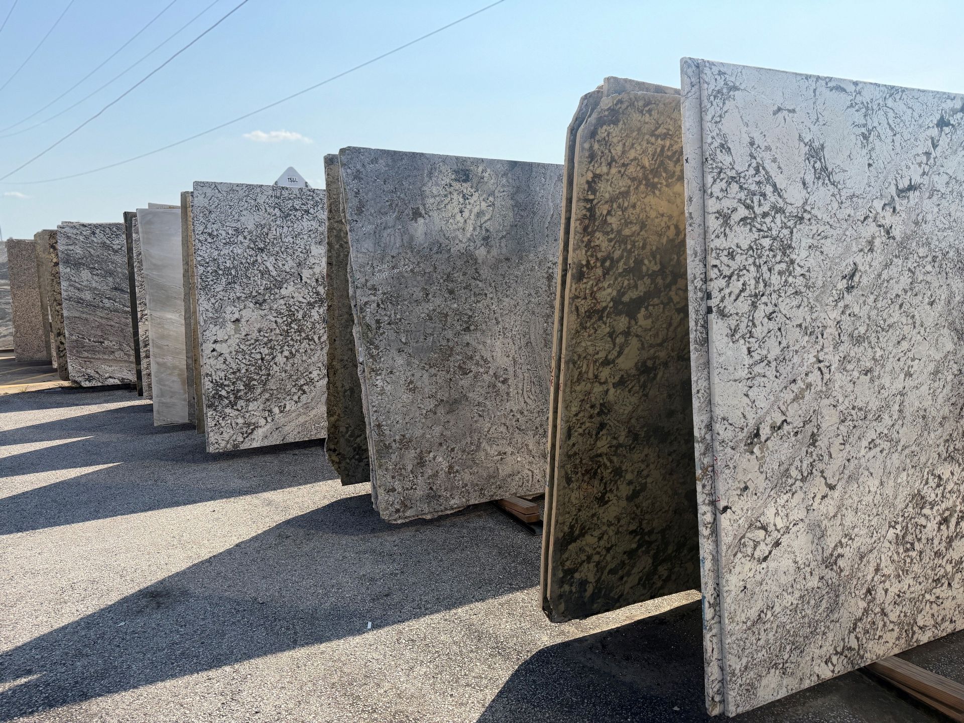 Large granite slabs standing upright outdoors in a row on a gravel surface.