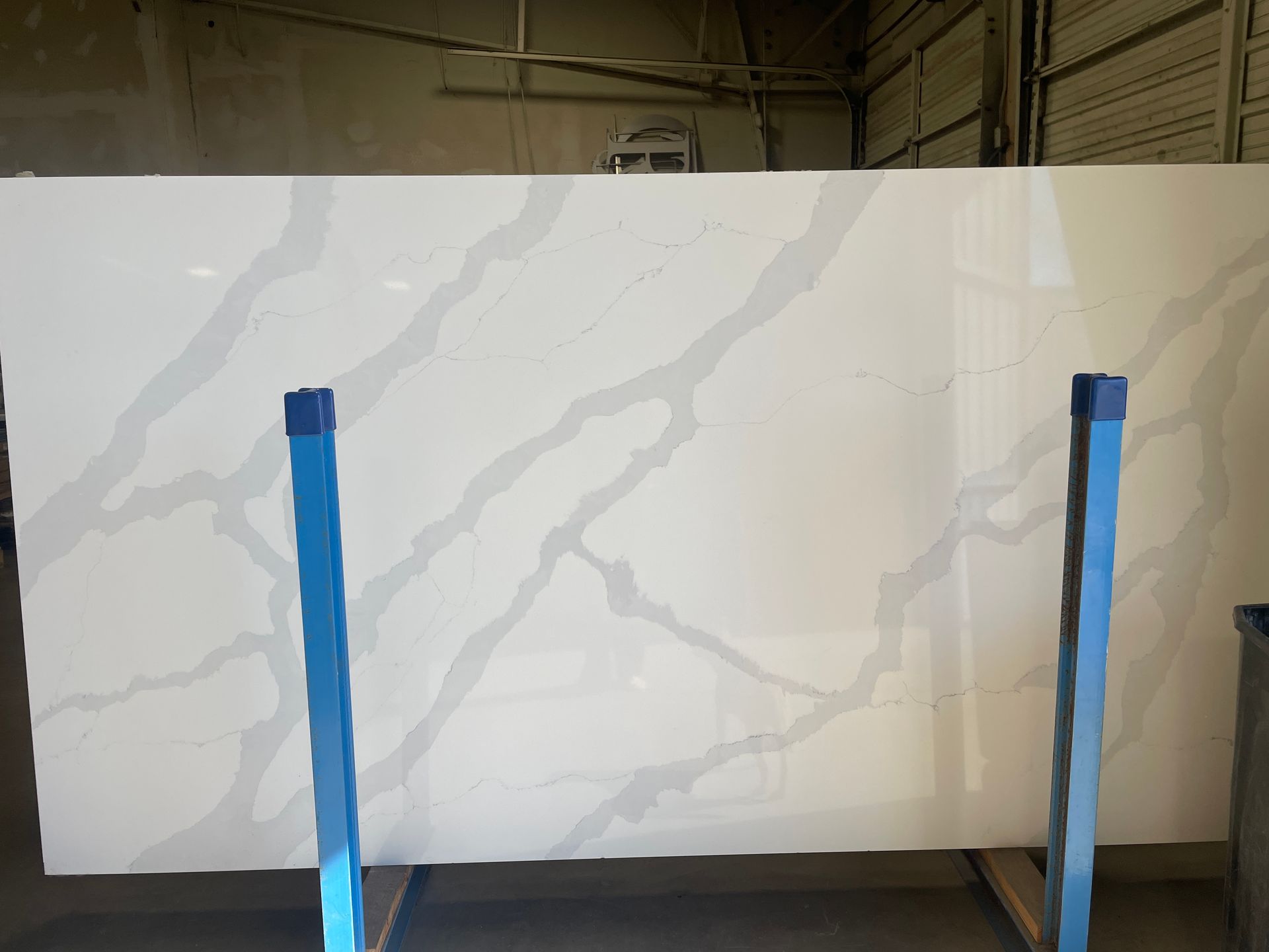 Large white marble-look slab standing on blue supports in an indoor workshop.