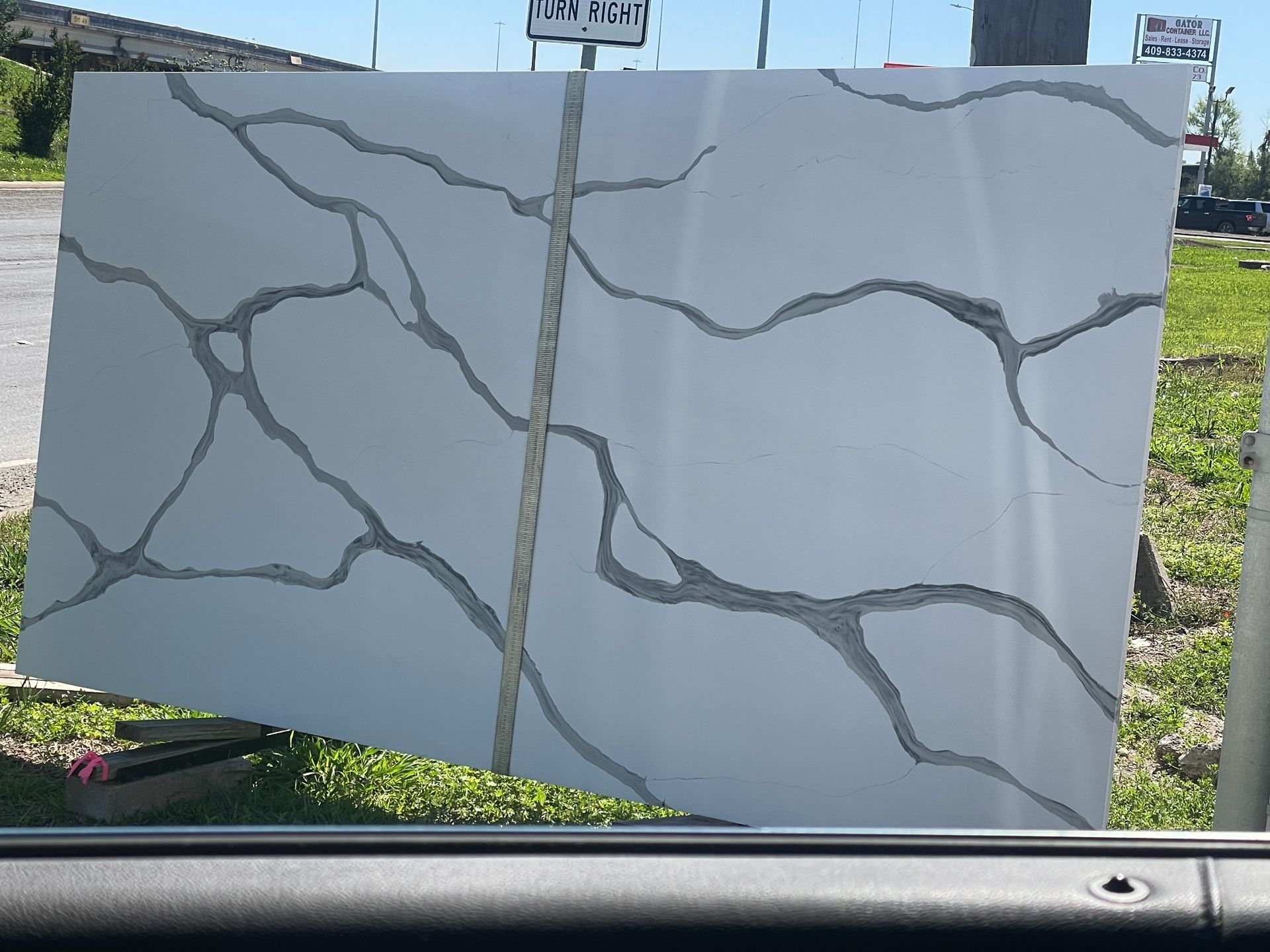 Large white stone slab with gray veining, displayed outdoors on grass beside a road.