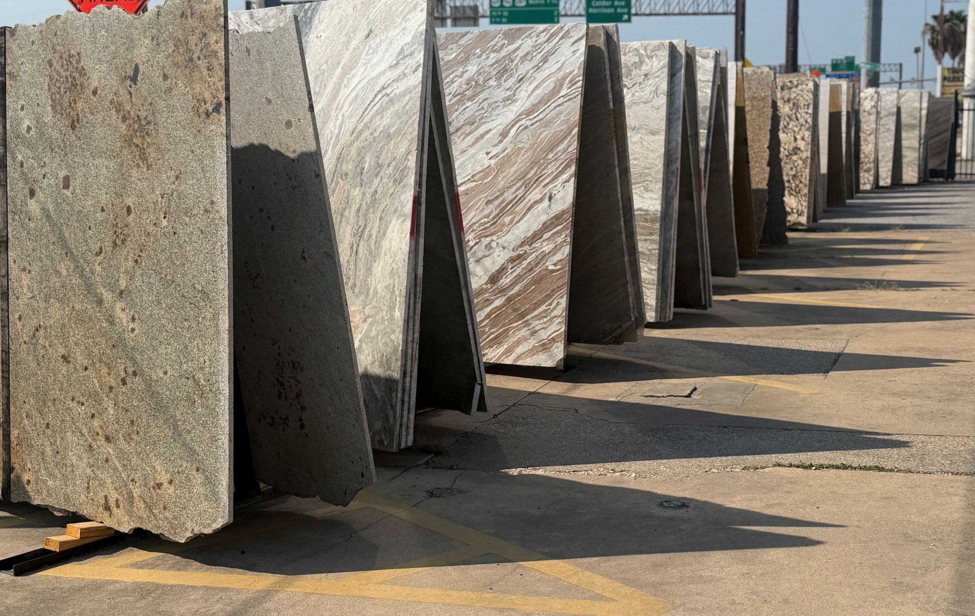 Rows of large stone slabs standing upright outdoors on a paved lot.