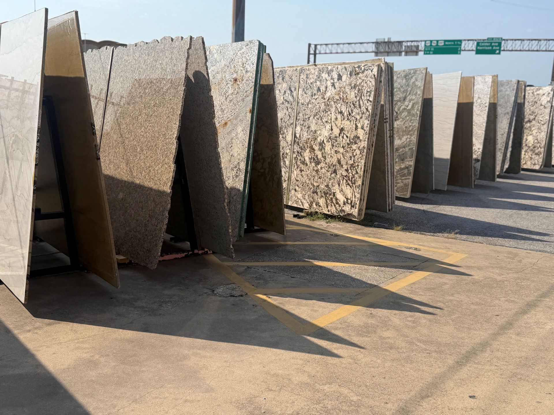 Large stone slabs leaning in a row along a sunlit roadside, with highway signs in the distance