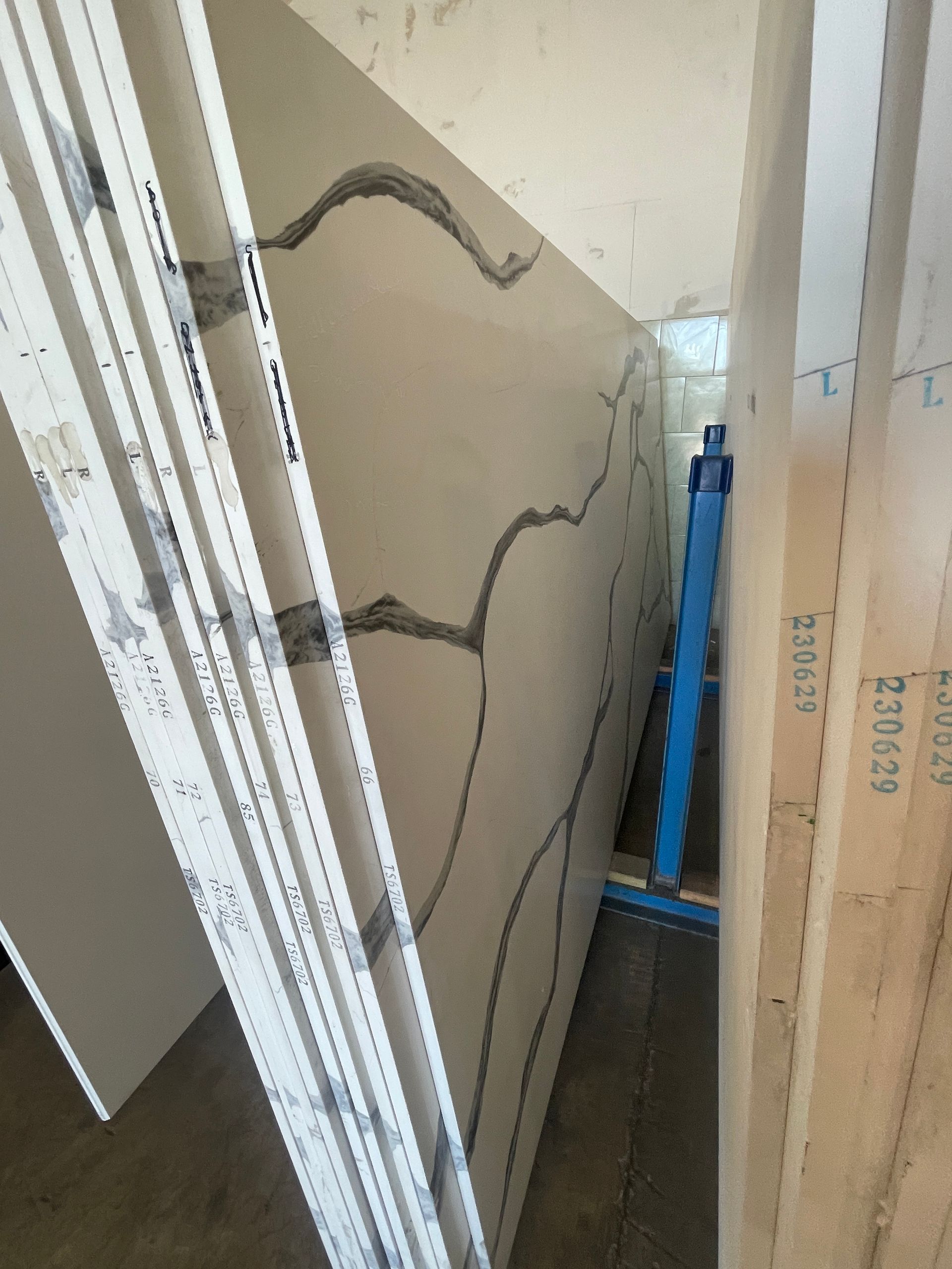 Cracked white wall panel leaning in a narrow space beside stacked materials, with a blue tool behind it.