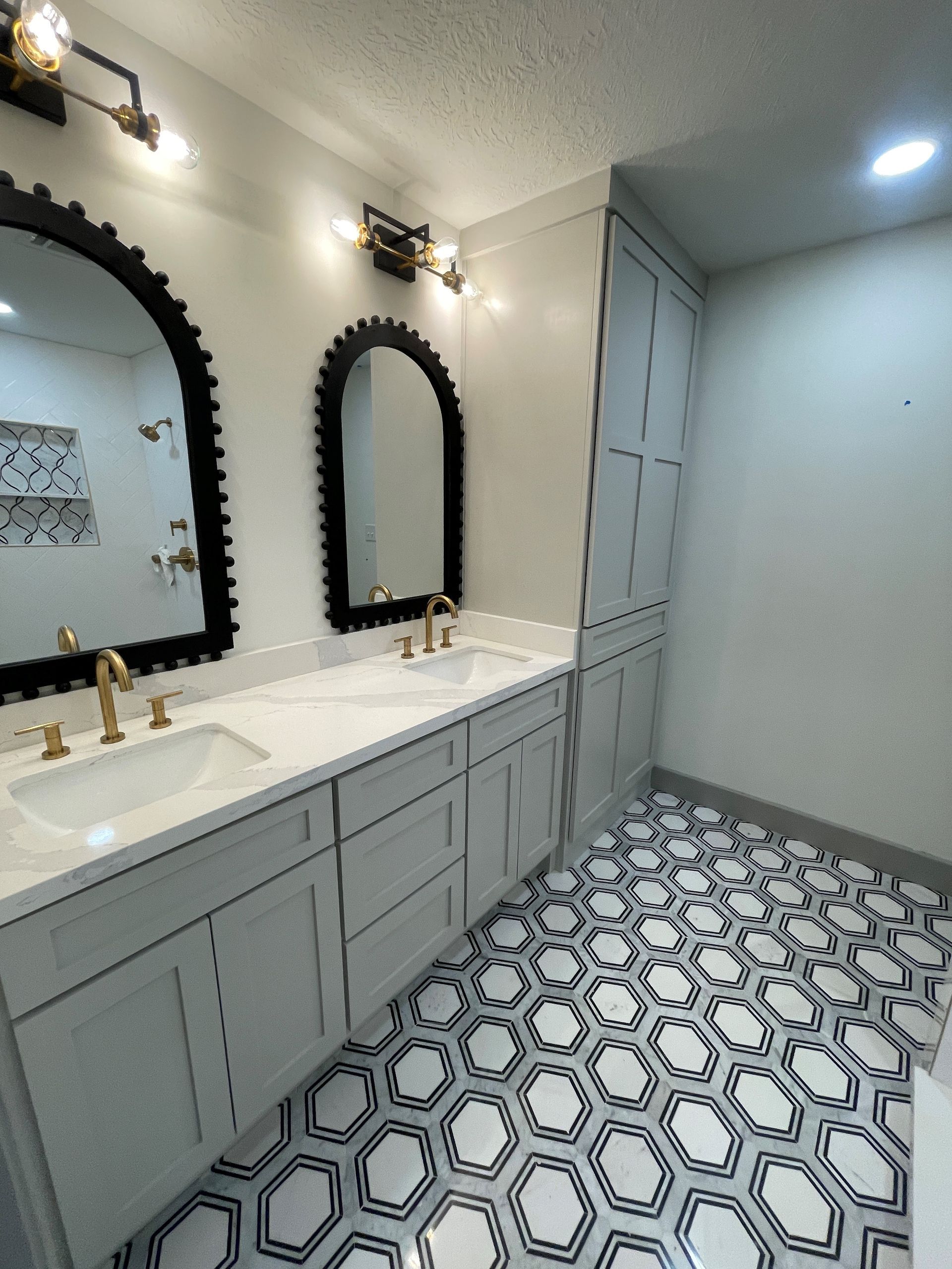 Modern bathroom vanity with double sinks, black mirrors, white cabinets, and patterned tile floor
