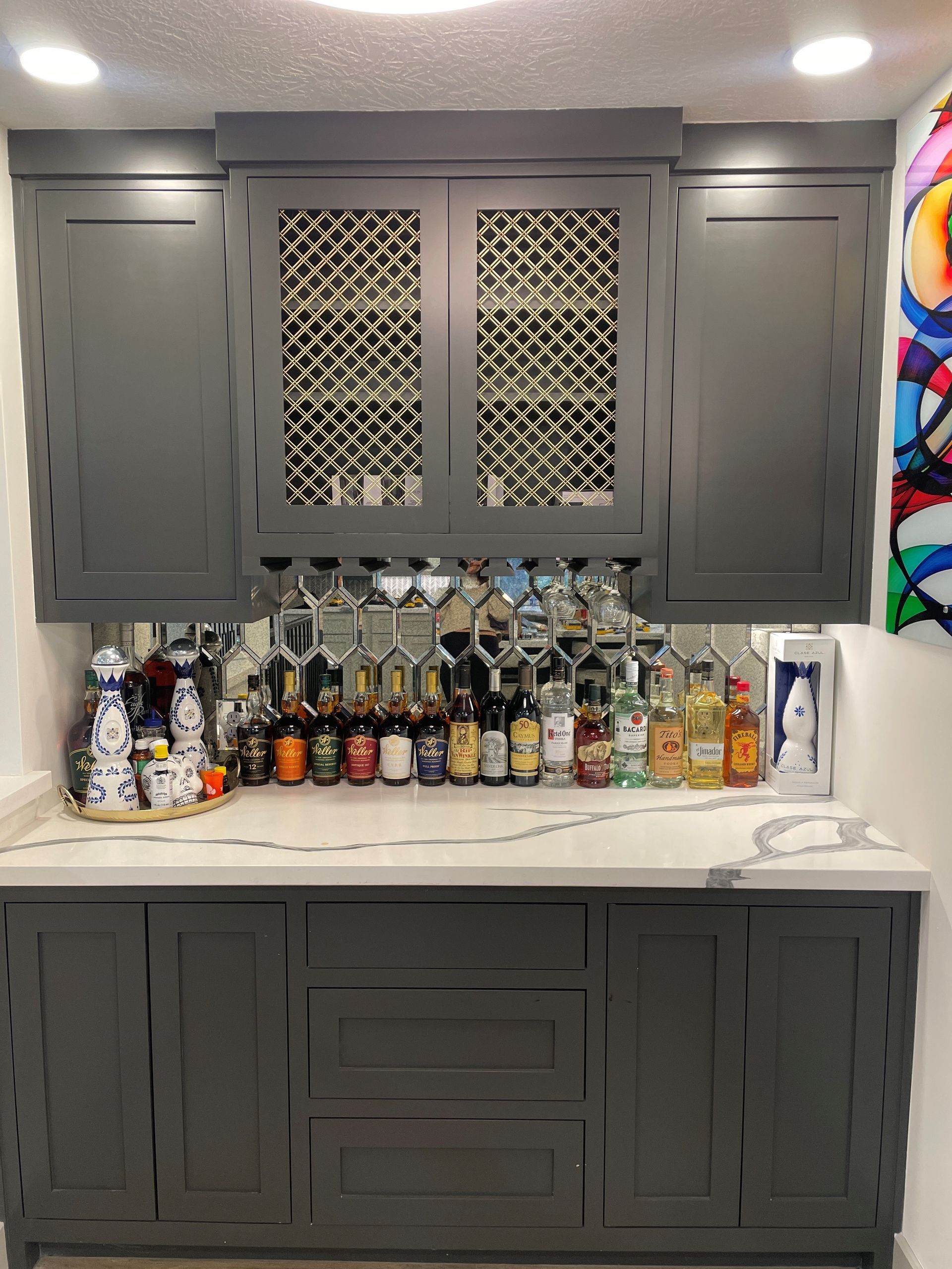 Gray kitchen wet bar with cabinets, mirrored backsplash, and assorted liquor bottles on the counter