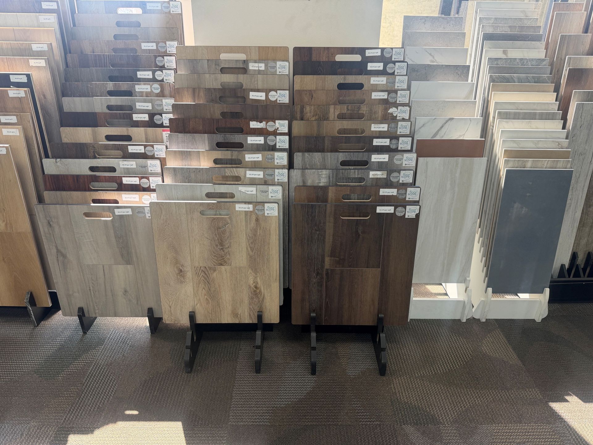 Display of wood and laminate flooring samples in a showroom, arranged in racks on carpeted floor.