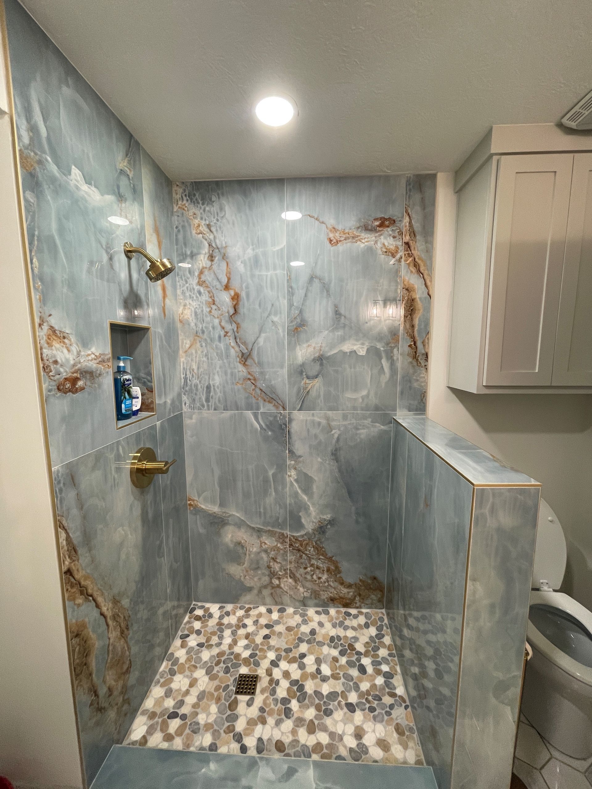Stone-tiled walk-in shower with marble-look walls, mosaic floor, and glass partition in a modern bathroom