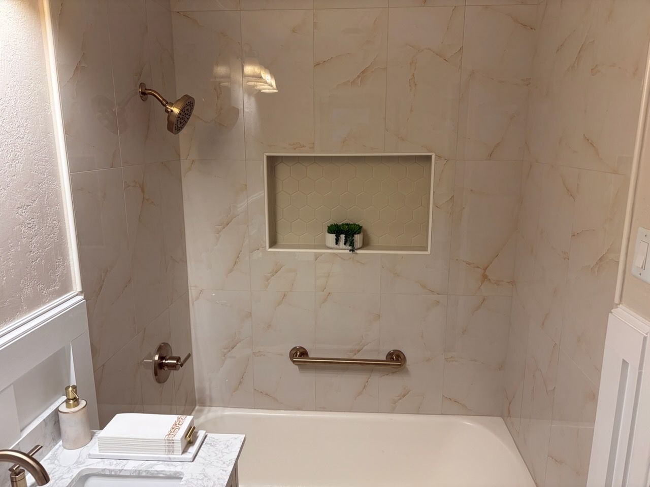 White tiled bathtub with chrome fixtures, built-in niche, and small green toy/soap in the shower wall alcove