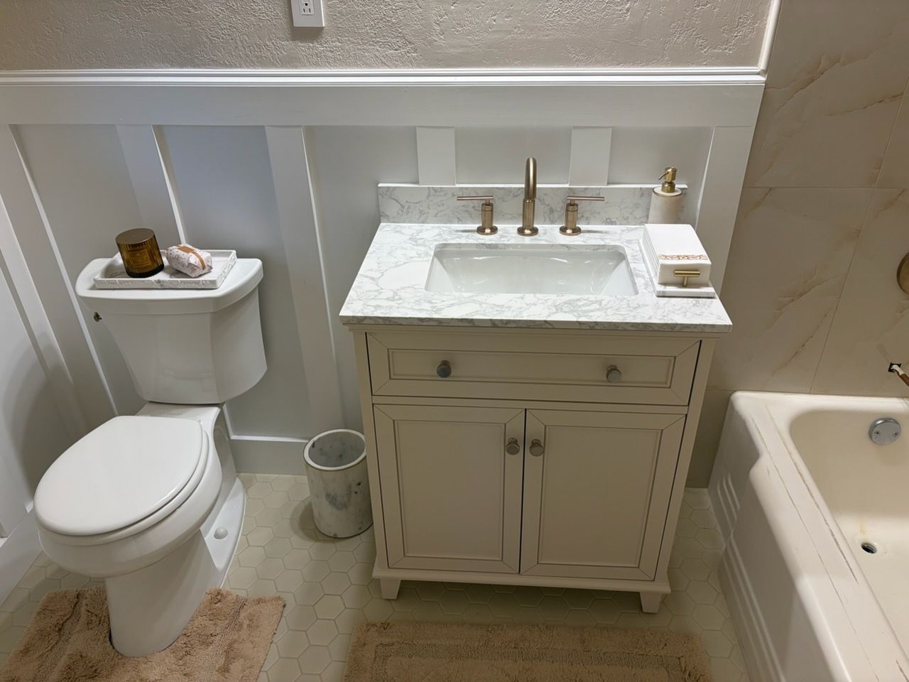 Small bathroom with toilet, vanity sink, tub, and neutral decor.