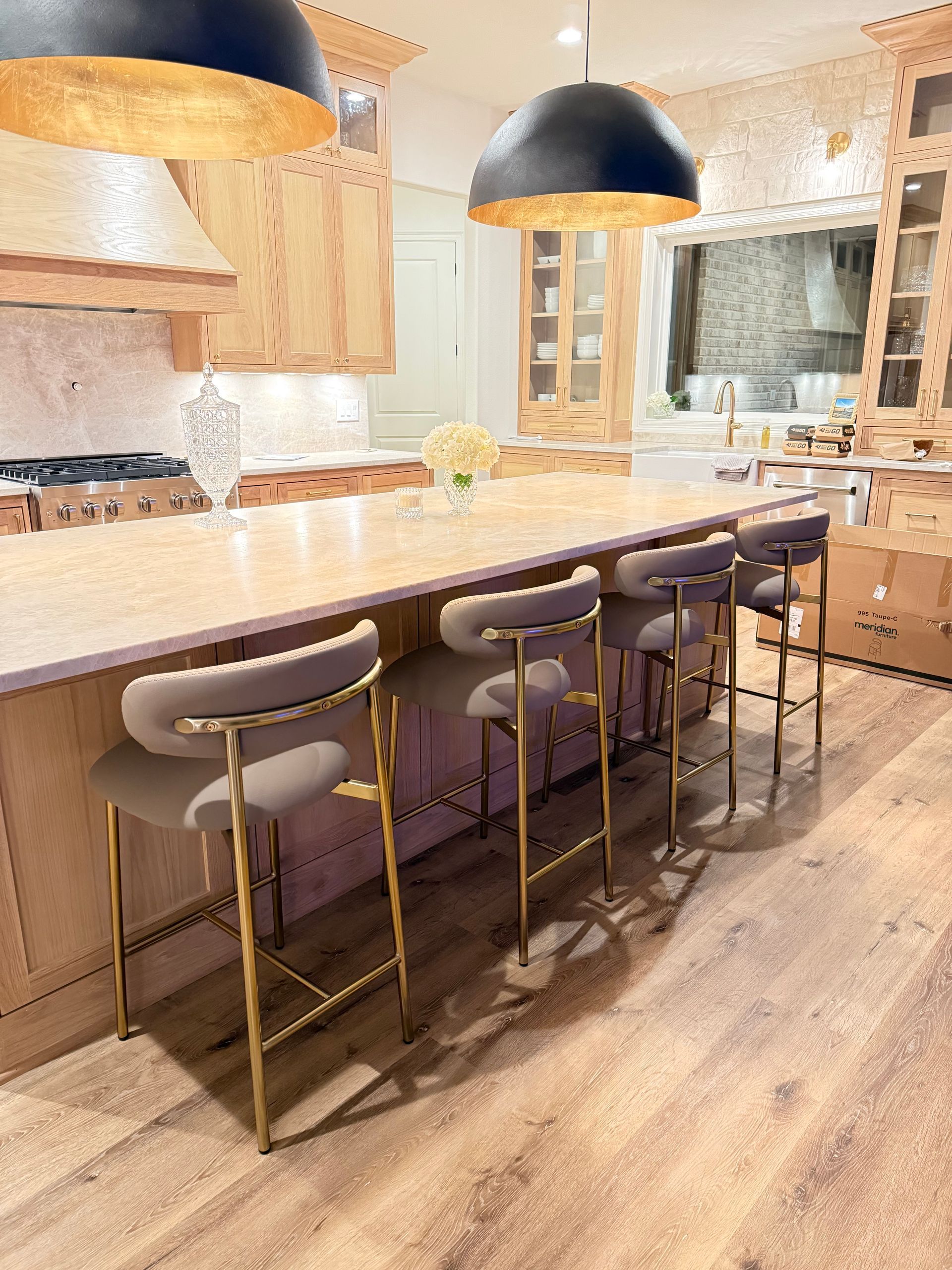 Modern kitchen with a large island, four stools, pendant lights, and warm wood cabinetry