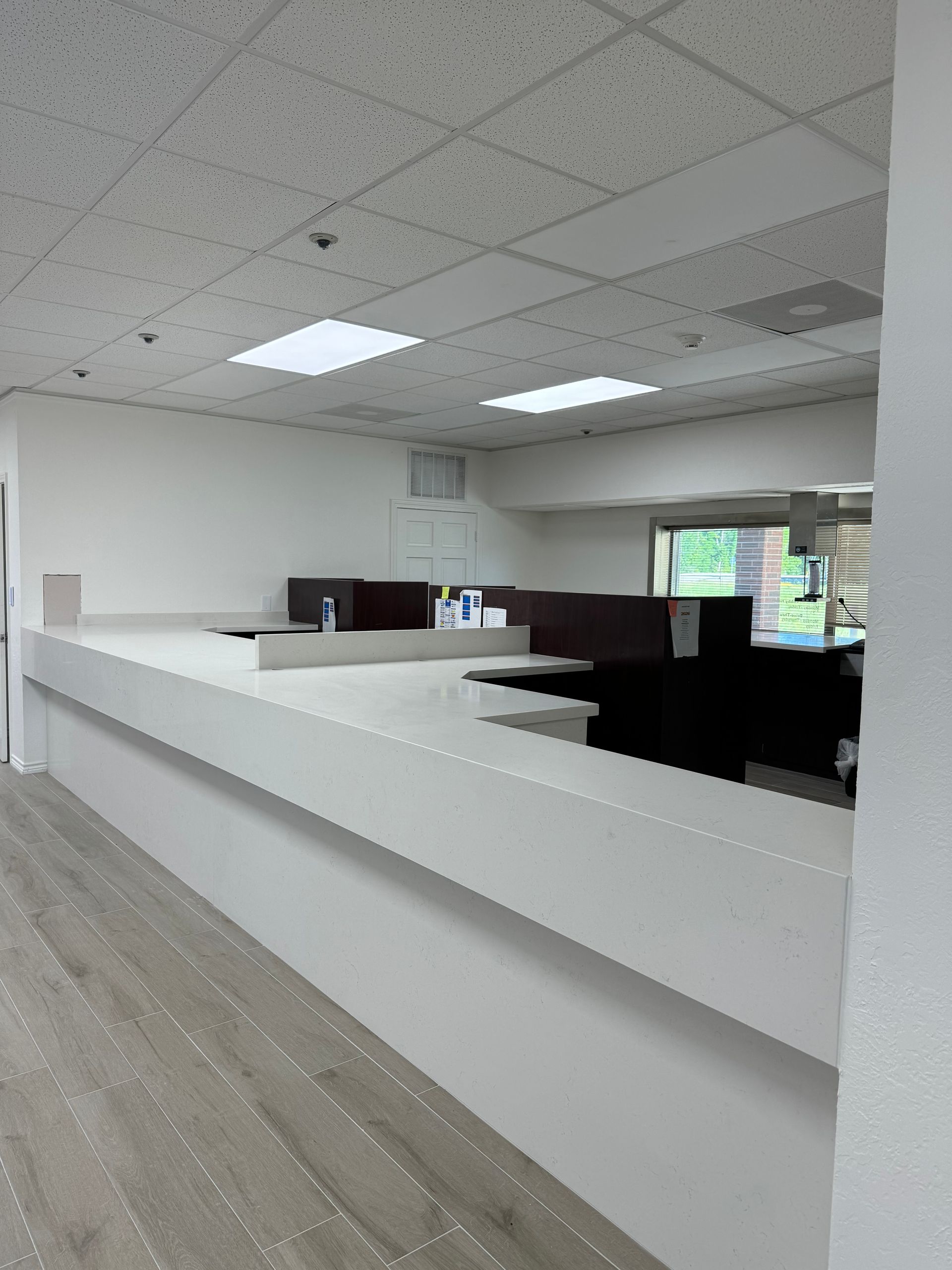 Empty office reception area with white partitions, drop ceiling, and wood flooring