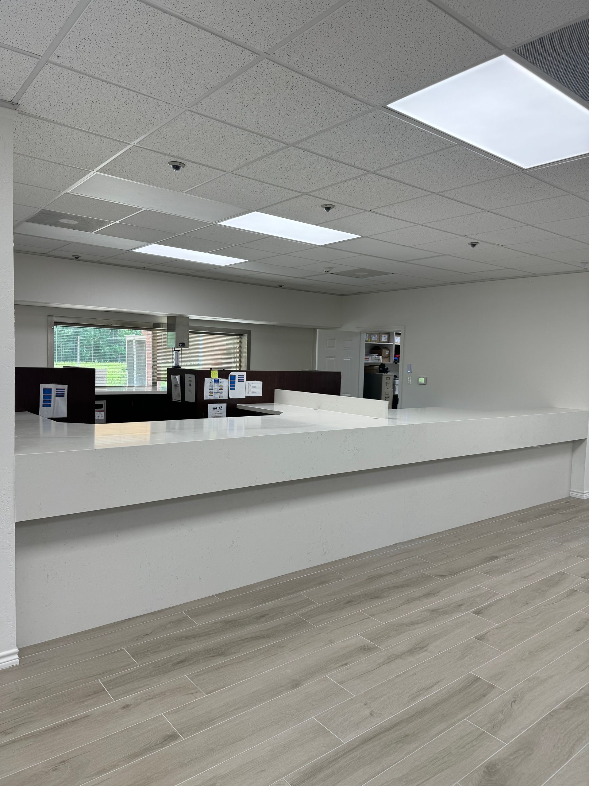 Empty modern office lobby with white reception desk, gray floor, and ceiling lights