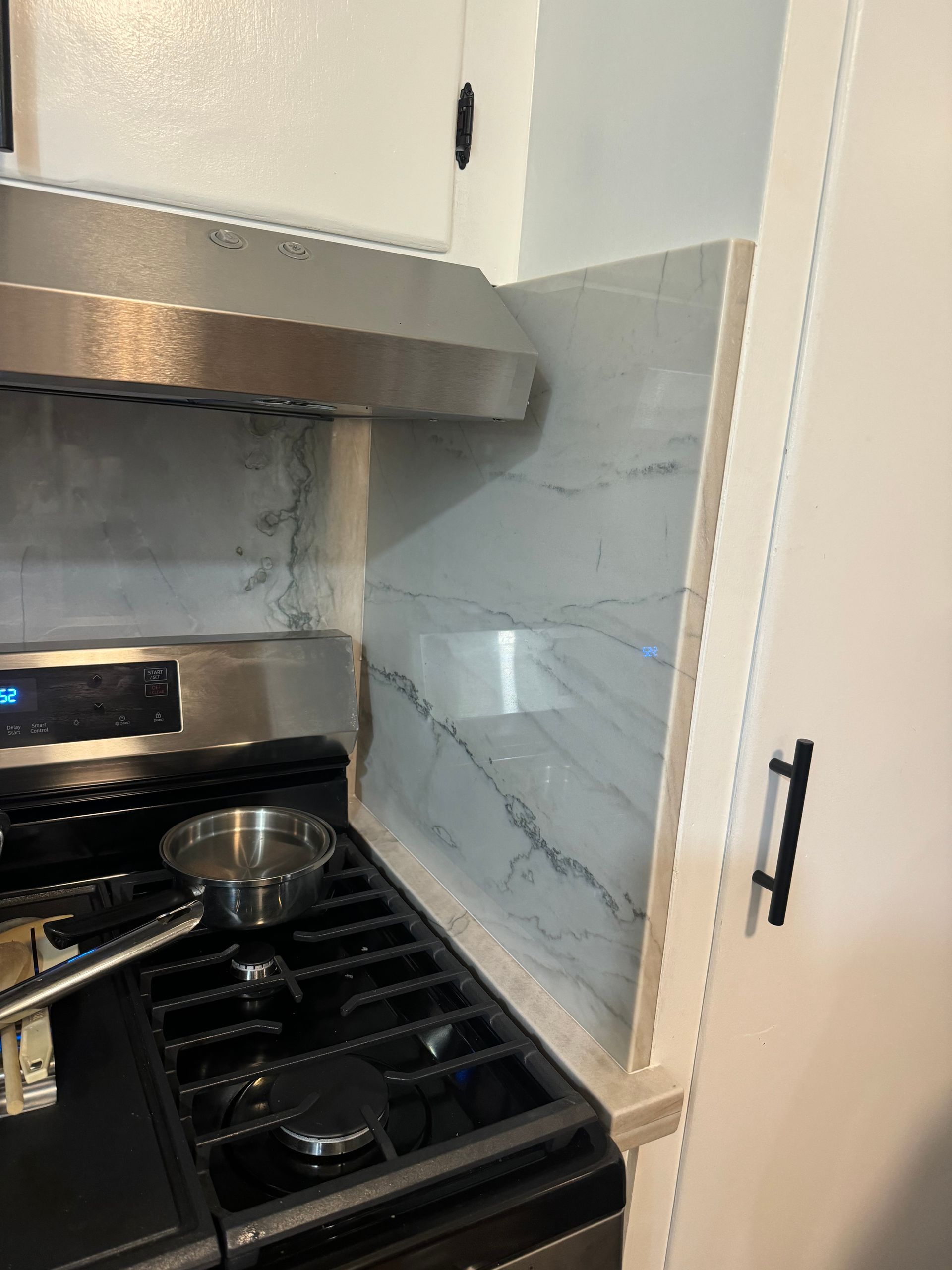Modern kitchen stove with metal pot under stainless range hood and marble backsplash