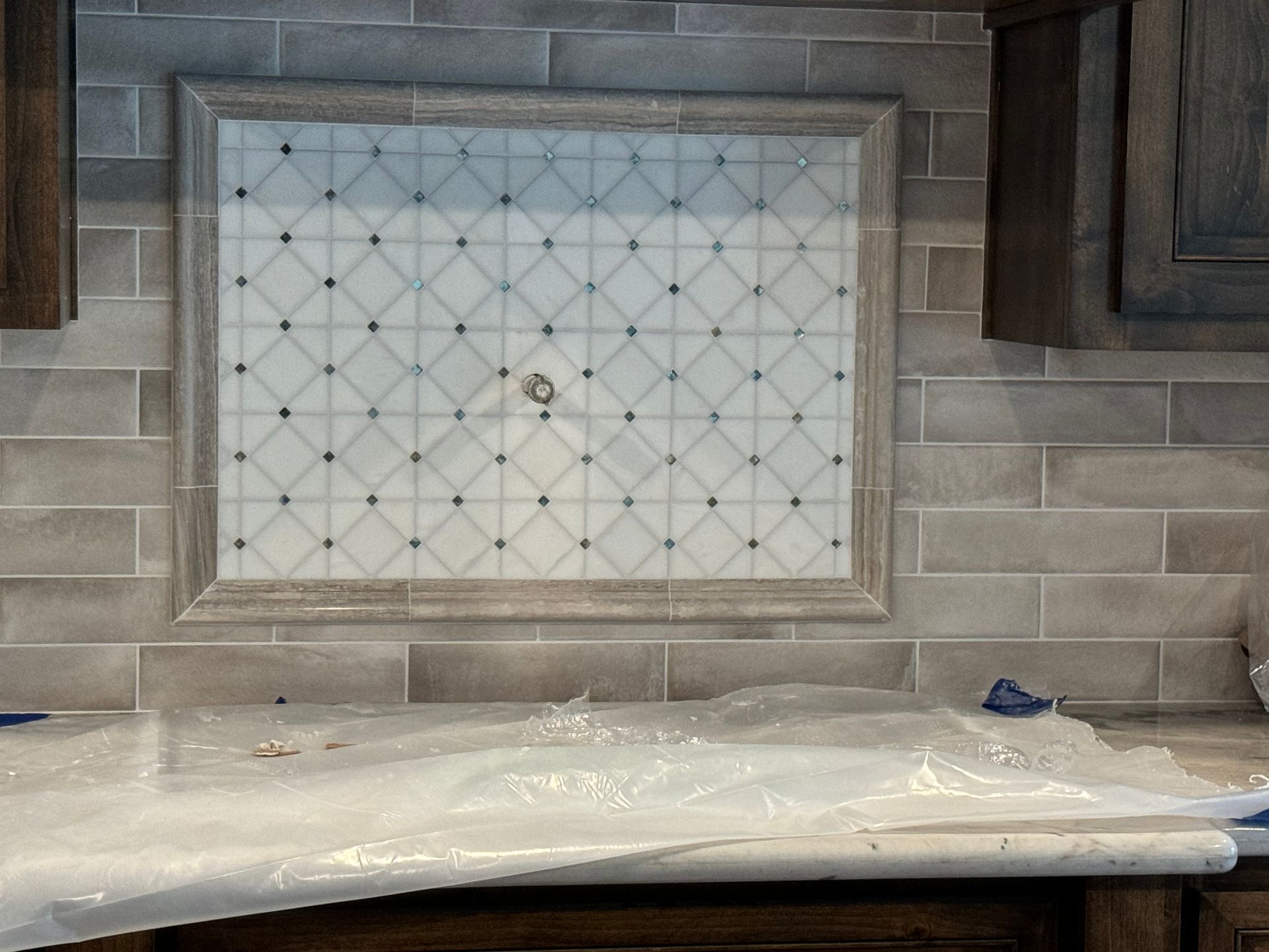 Kitchen backsplash with white tile insert, gray subway tiles, and a countertop covered in protective plastic.