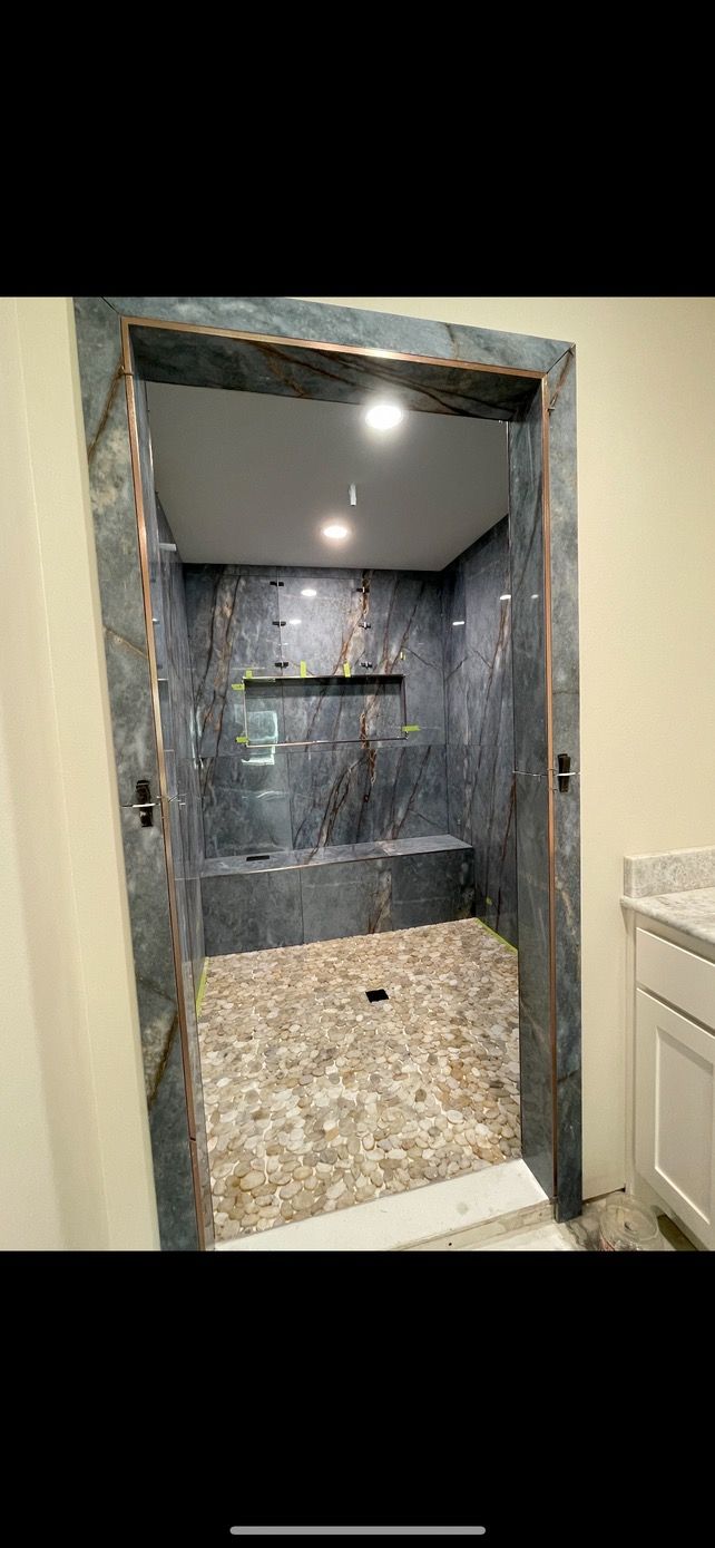 Tiled shower stall with stone-pattern walls, recessed shelf, and pebble floor seen through a doorway