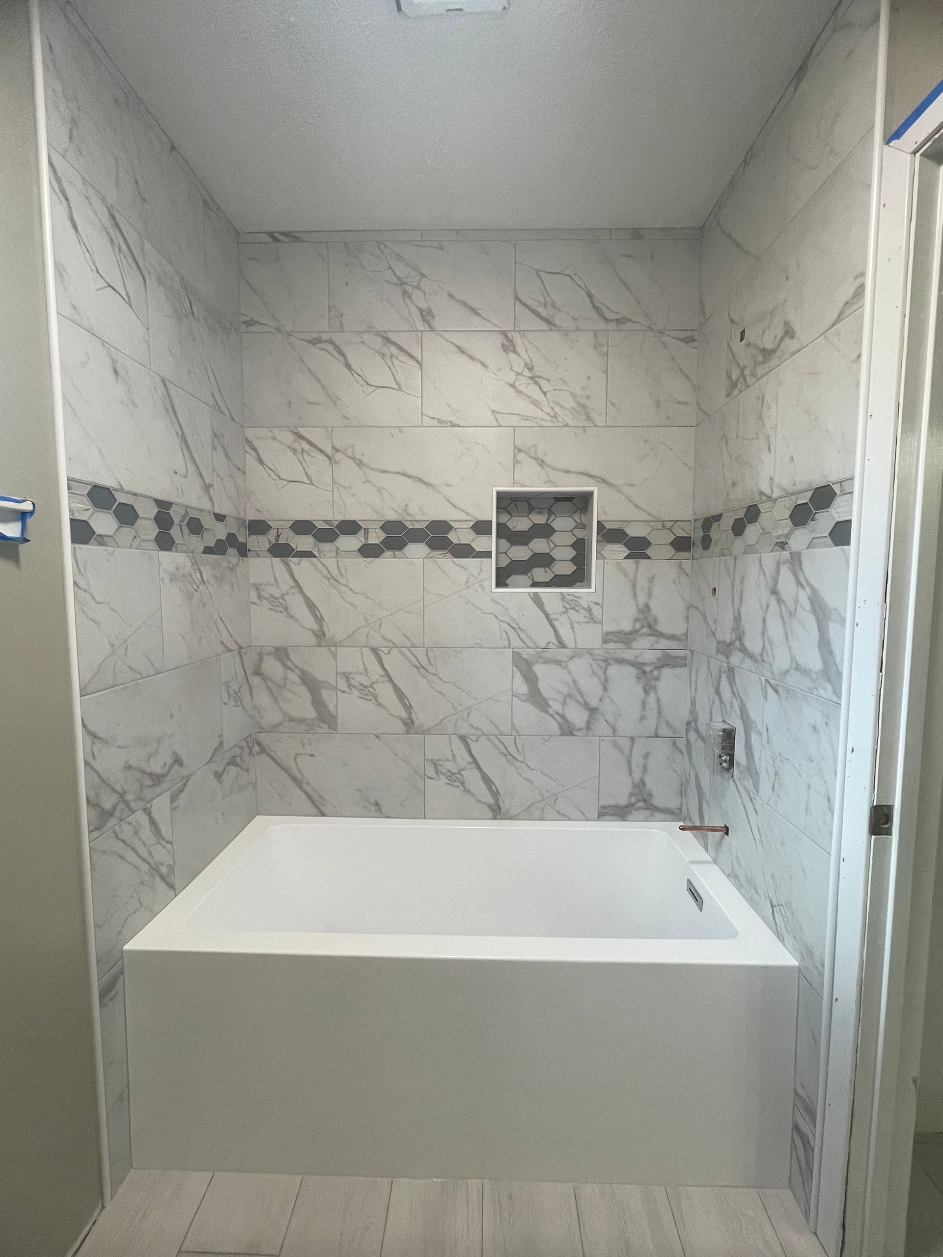 Small tiled bathroom with a deep rectangular soaking tub and marble-pattern walls.
